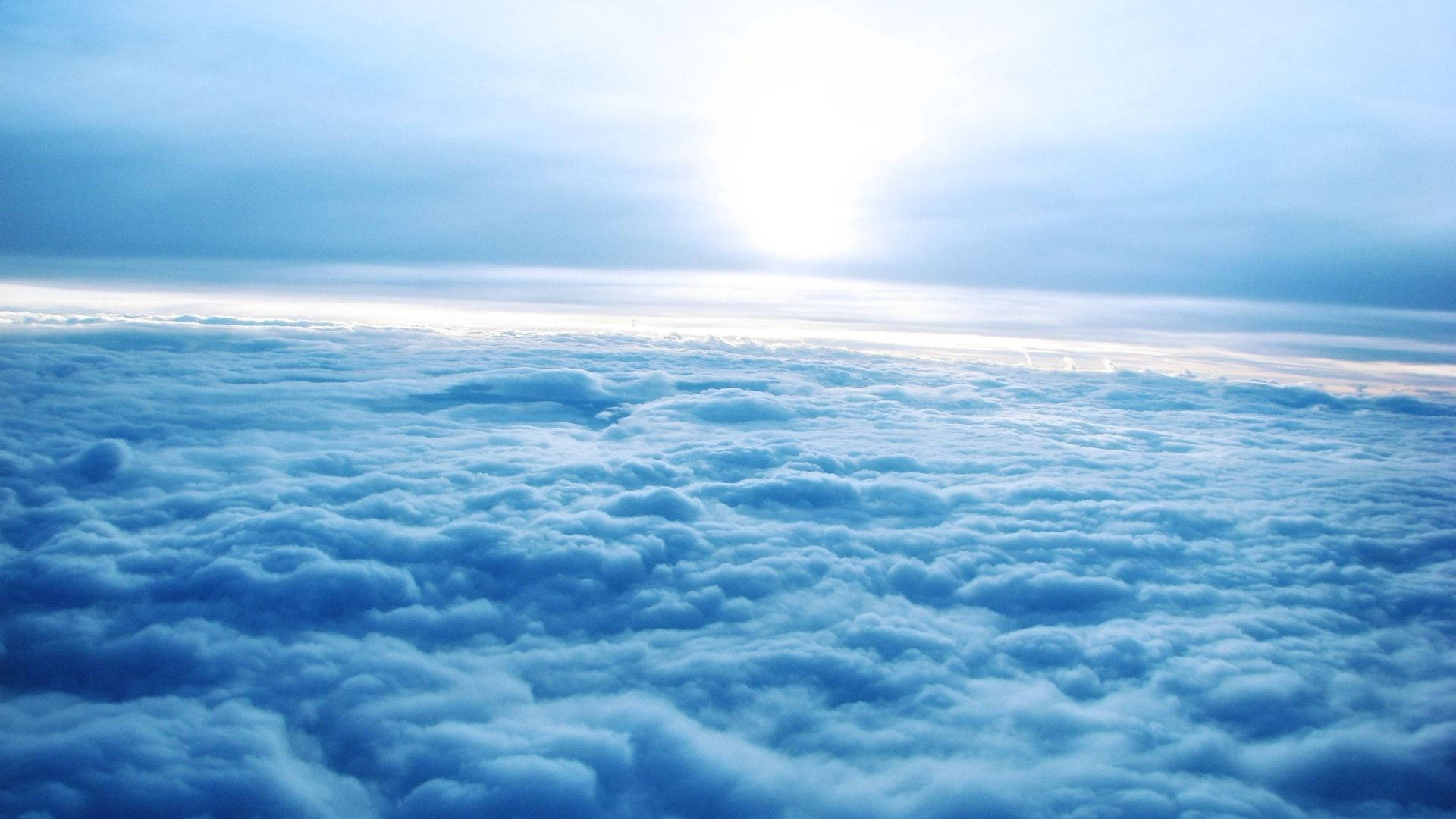 雲層覆蓋天空景觀 壁紙 — 從上方俯瞰，寧靜的航拍視角，無盡的藍色雲朵沐浴在柔和的陽光中。
