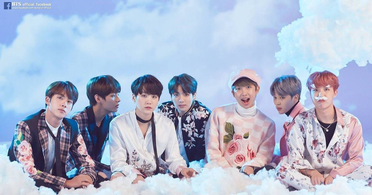 七位身穿花卉服裝的 K-pop 偶像坐在雲朵上，表情愉快。