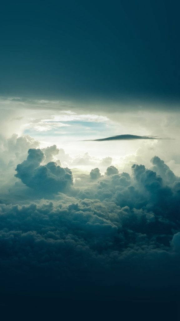 雲朵自然 iPhone 背景 壁紙 — 戲劇性的雲層被陽光穿透暴風雨的天空照亮，下方是無盡的蓬鬆白色和灰色雲海。