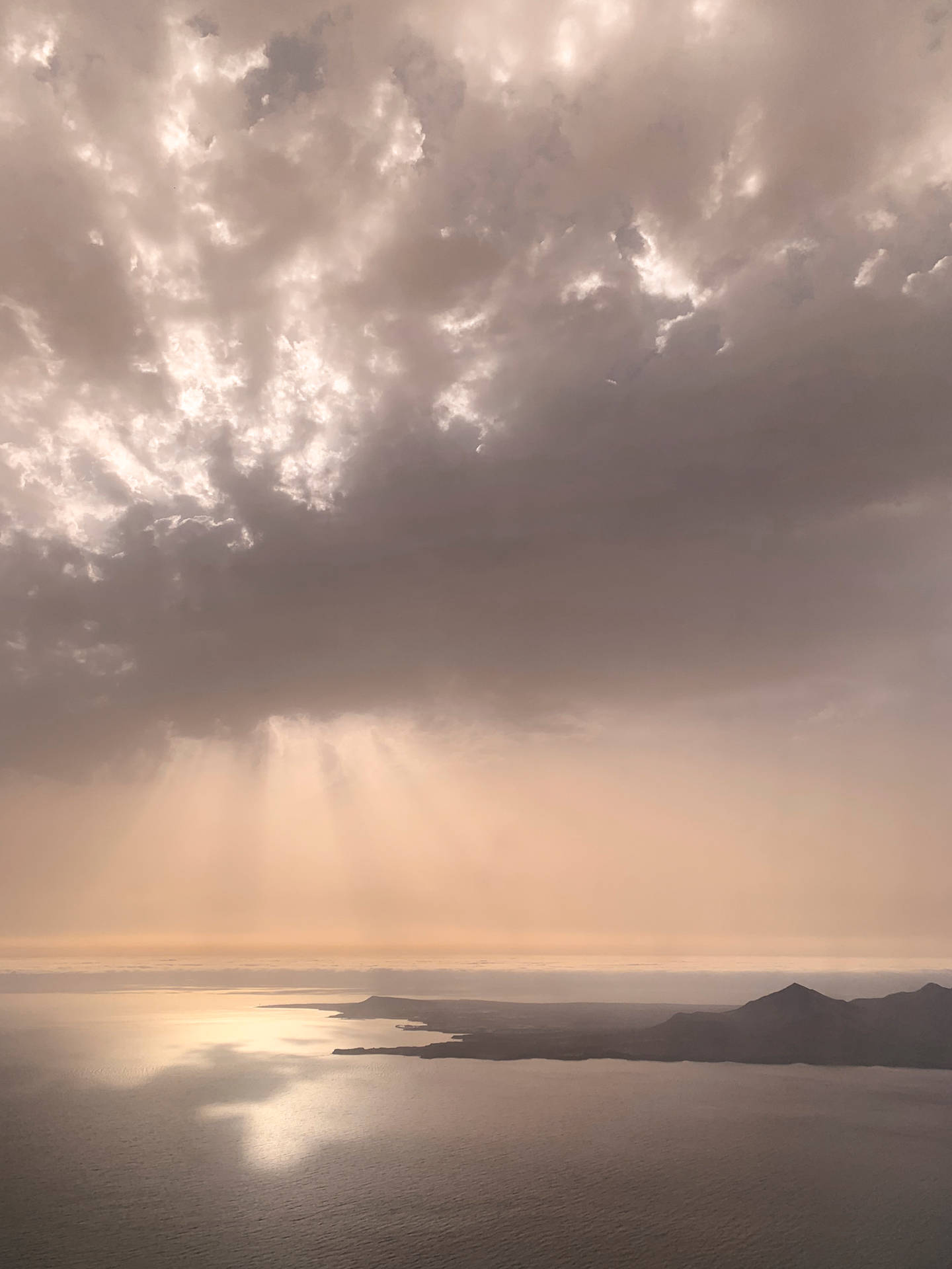陽光穿過暴風雲，照耀在平靜的海面和遠處的陸地上。