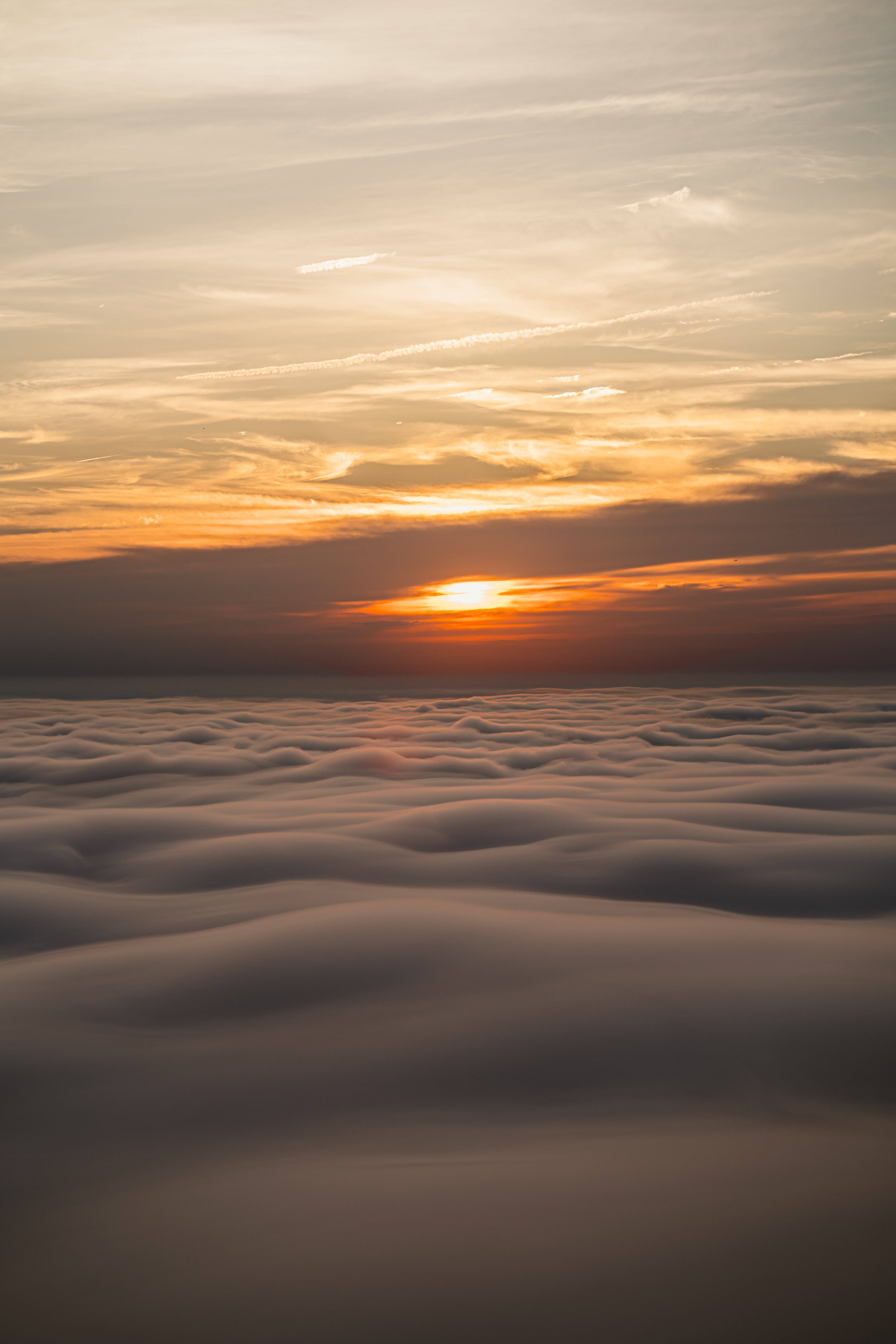 雲海背景 壁紙 — 夕陽以溫暖的橙色和金色塗抹天空，沉入柔軟翻滾的雲海之下。