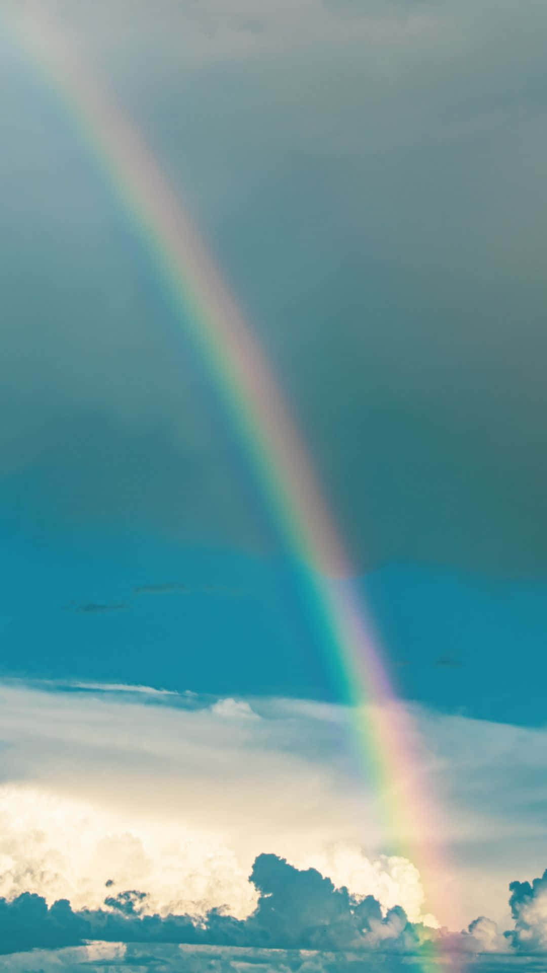 一道清晰的彩虹橫跨多雲的天空，帶有藍色和白色色調。
