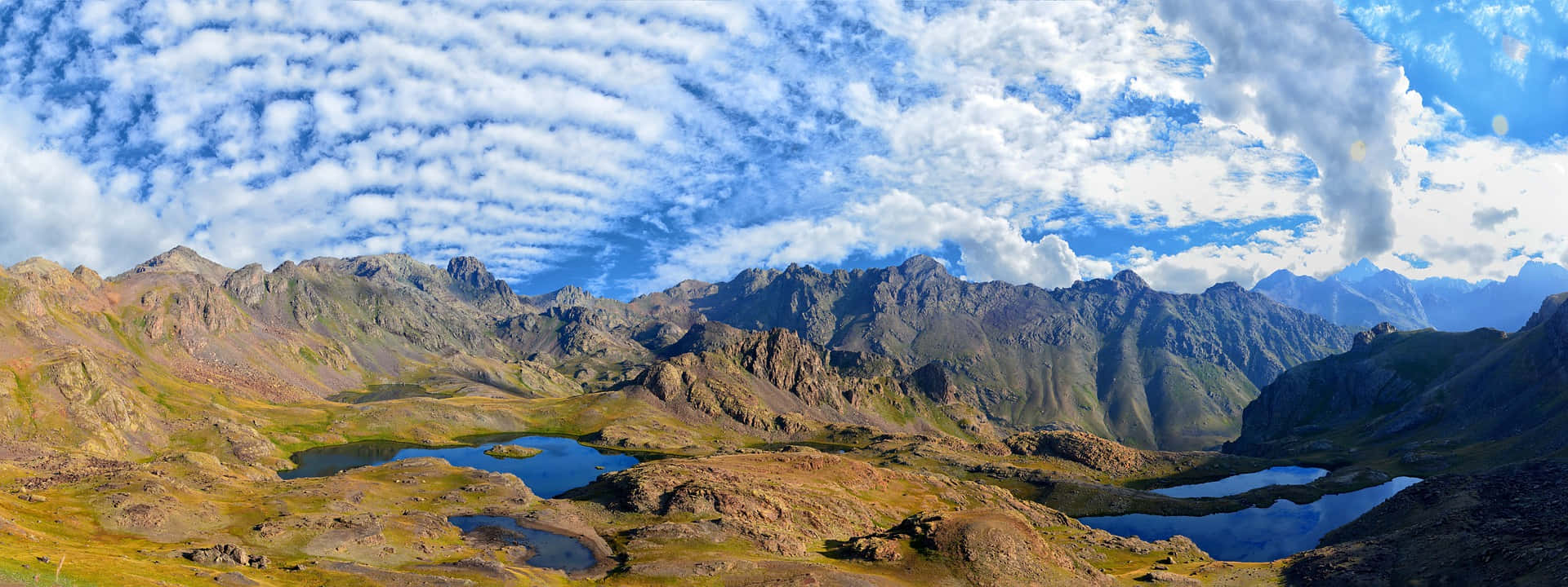 在明亮的藍天和零星白雲下，有高山湖泊的崎嶇山脈。