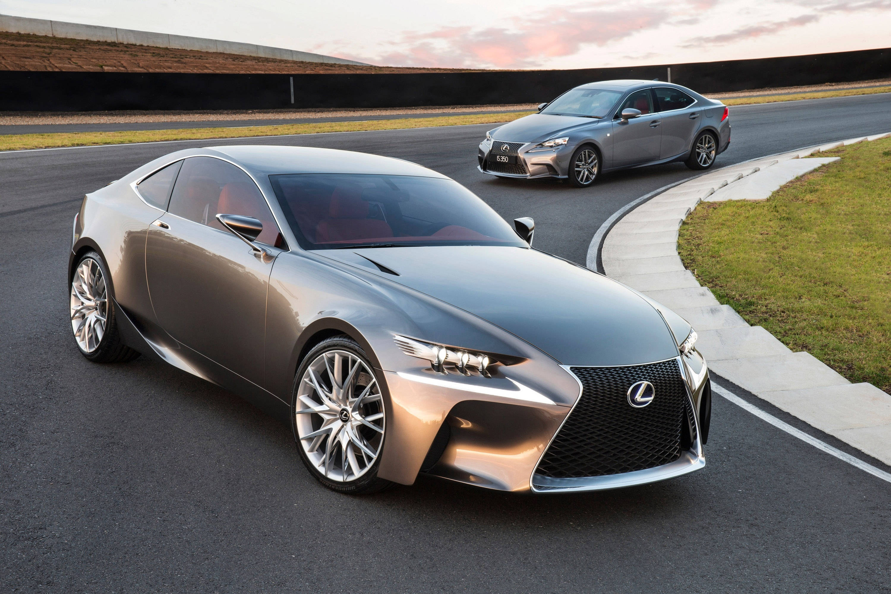 雷克薩斯LF-CC與IS 350 壁紙 — 兩輛時尚的銀色 Lexus 跑車在日落時分沿著蜿蜒的賽道滑行，天空呈現溫暖色調。