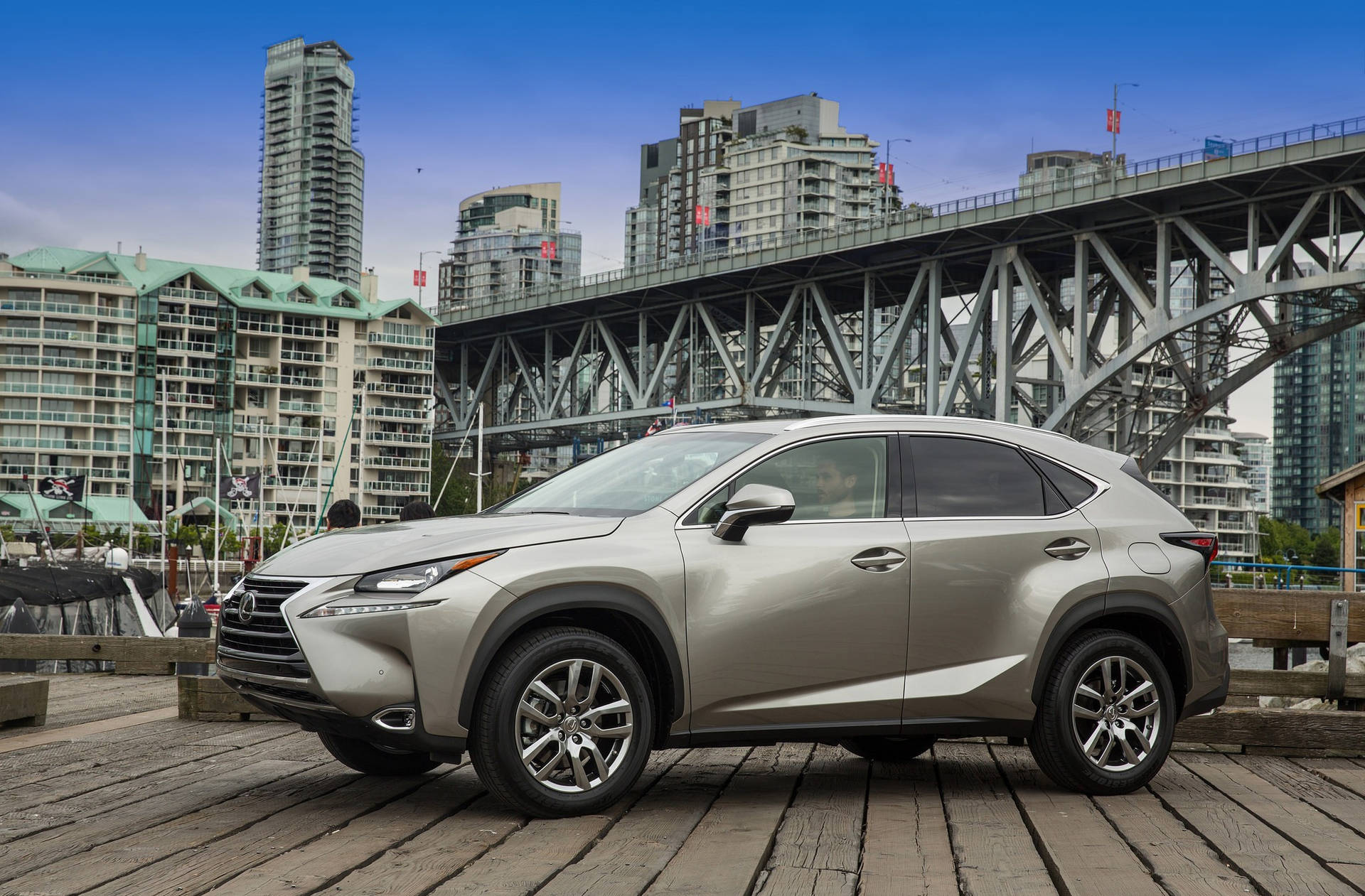 銀色Lexus NX SUV在木碼頭上，背後有城市橋樑和天際線。