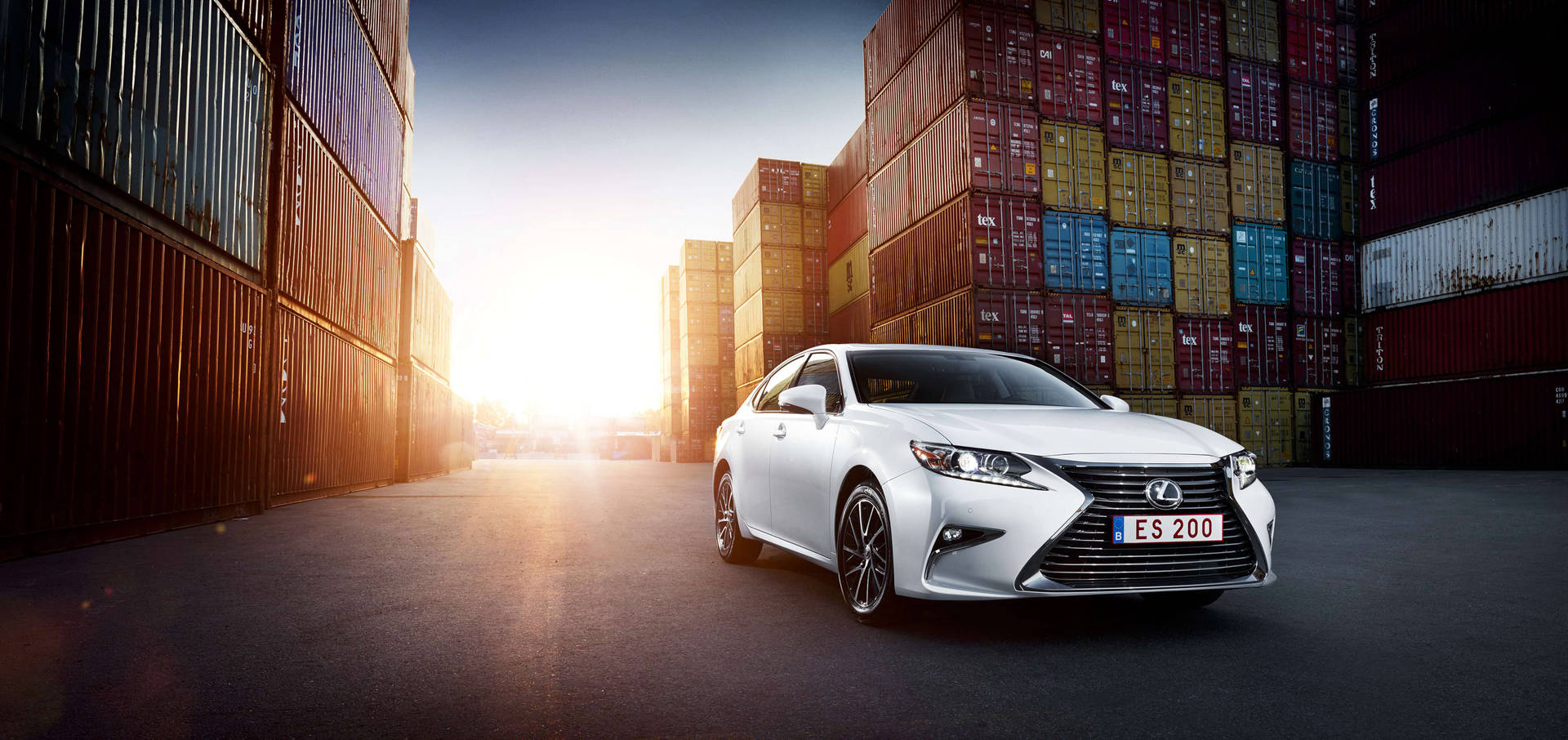 白色Lexus ES 200轎車停放在堆疊的貨運集裝箱之間，夕陽西下。