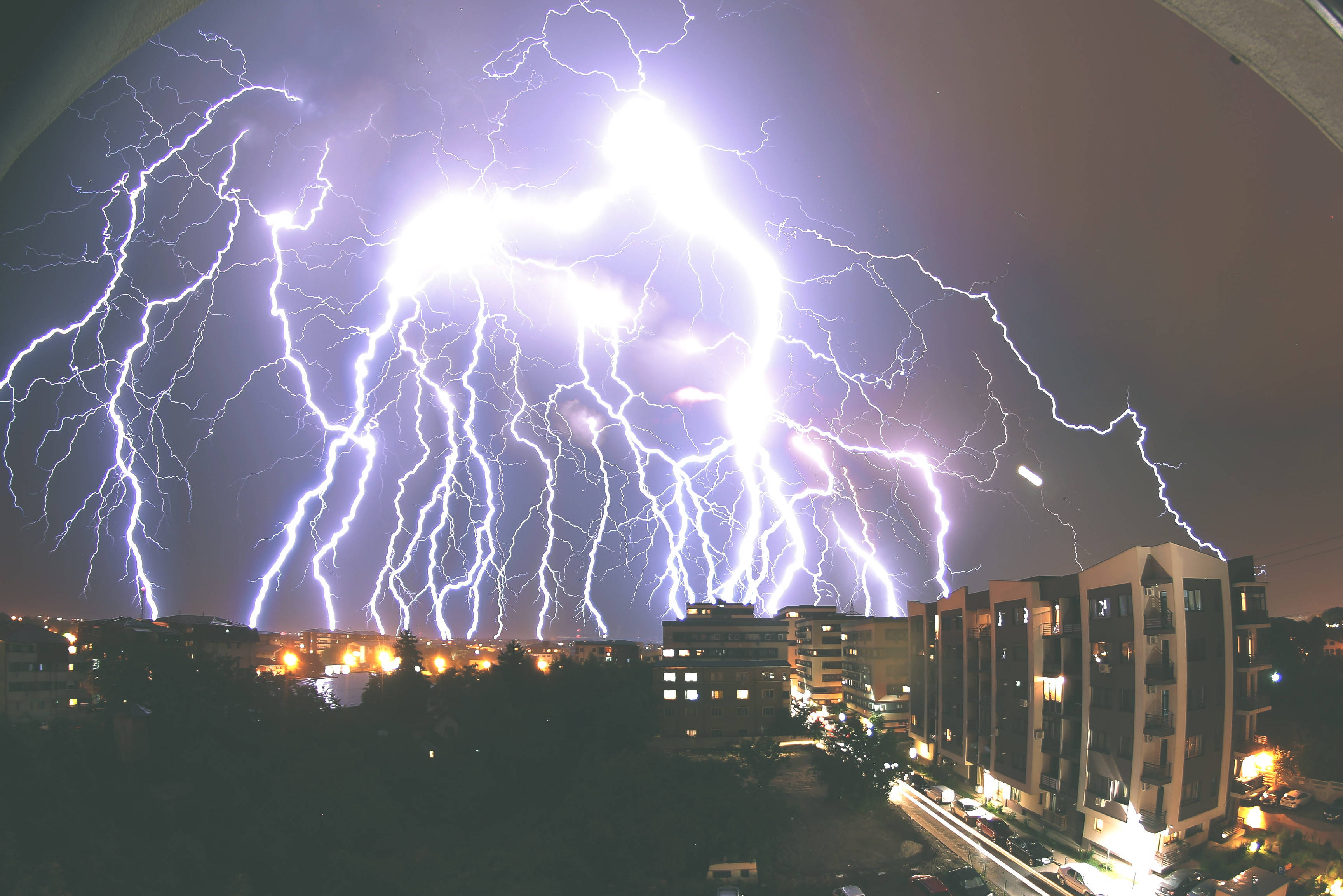 雷暴夜空城市 壁紙 — 巨大的閃電照亮了暴風雨夜晚的城市天際線，建築窗戶閃爍著光芒。