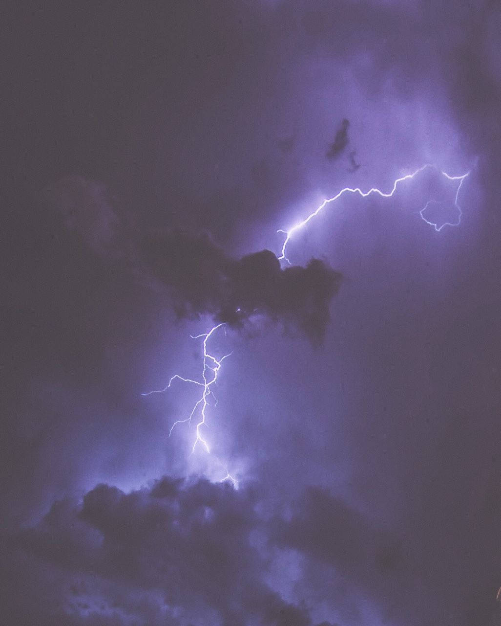 紫色閃電在夜間穿過黑暗的暴風雲閃爍。