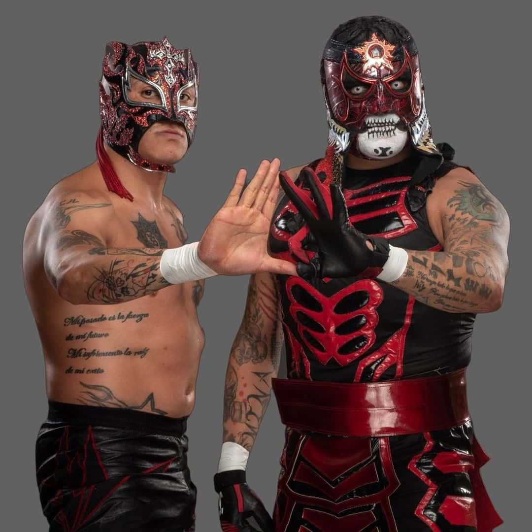 雷芬希與潘塔零M組成Lucha Brothers 壁紙 — 兩名戴面具的摔角手身穿紅色和黑色裝備，在灰色工作室背景前展示紋身手臂擺姿勢。