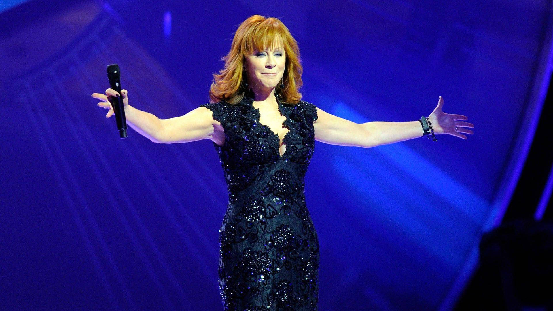歌手 Reba McEntire 在舞台上穿著黑色亮片連衣裙，雙臂伸展表演。