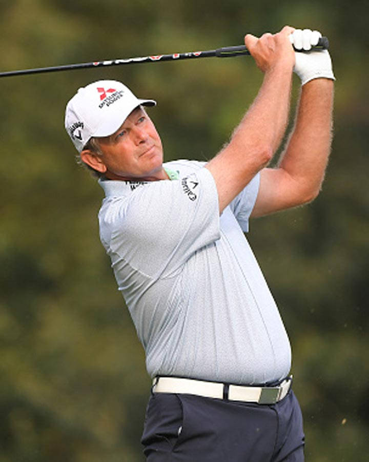 雷蒂夫·古森 - Callaway Apparel 大使 壁紙 — 一名男性高爾夫球手正處於揮桿動作中，專注而強烈，背景是模糊的綠色森林。