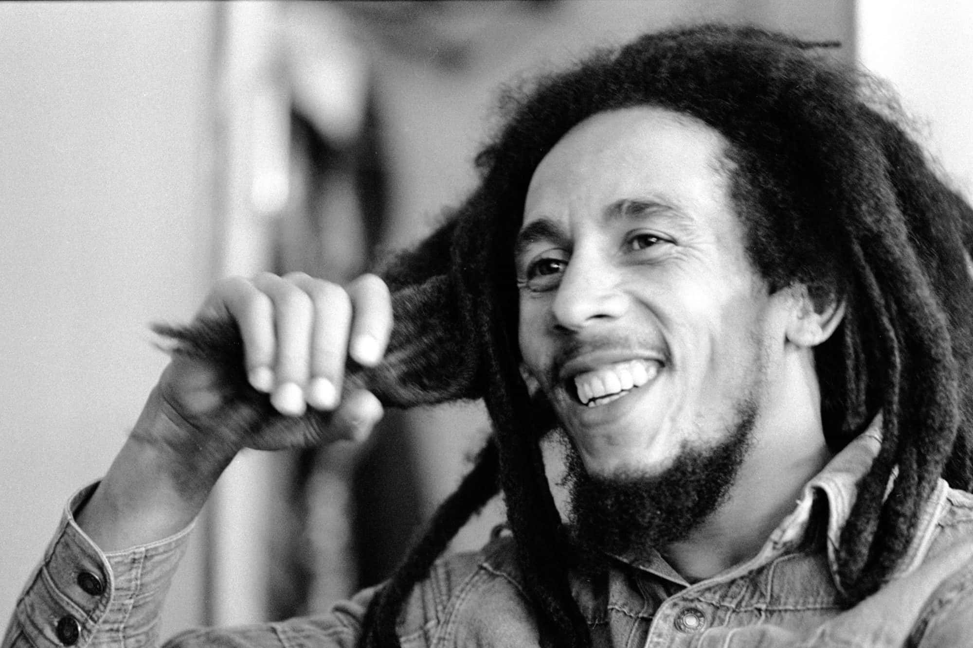 雷鬼之王——鮑勃·馬利 壁紙 — Bob Marley 在黑白真誠肖像中，開心地笑著，同時頑皮地觸摸他的辮子。