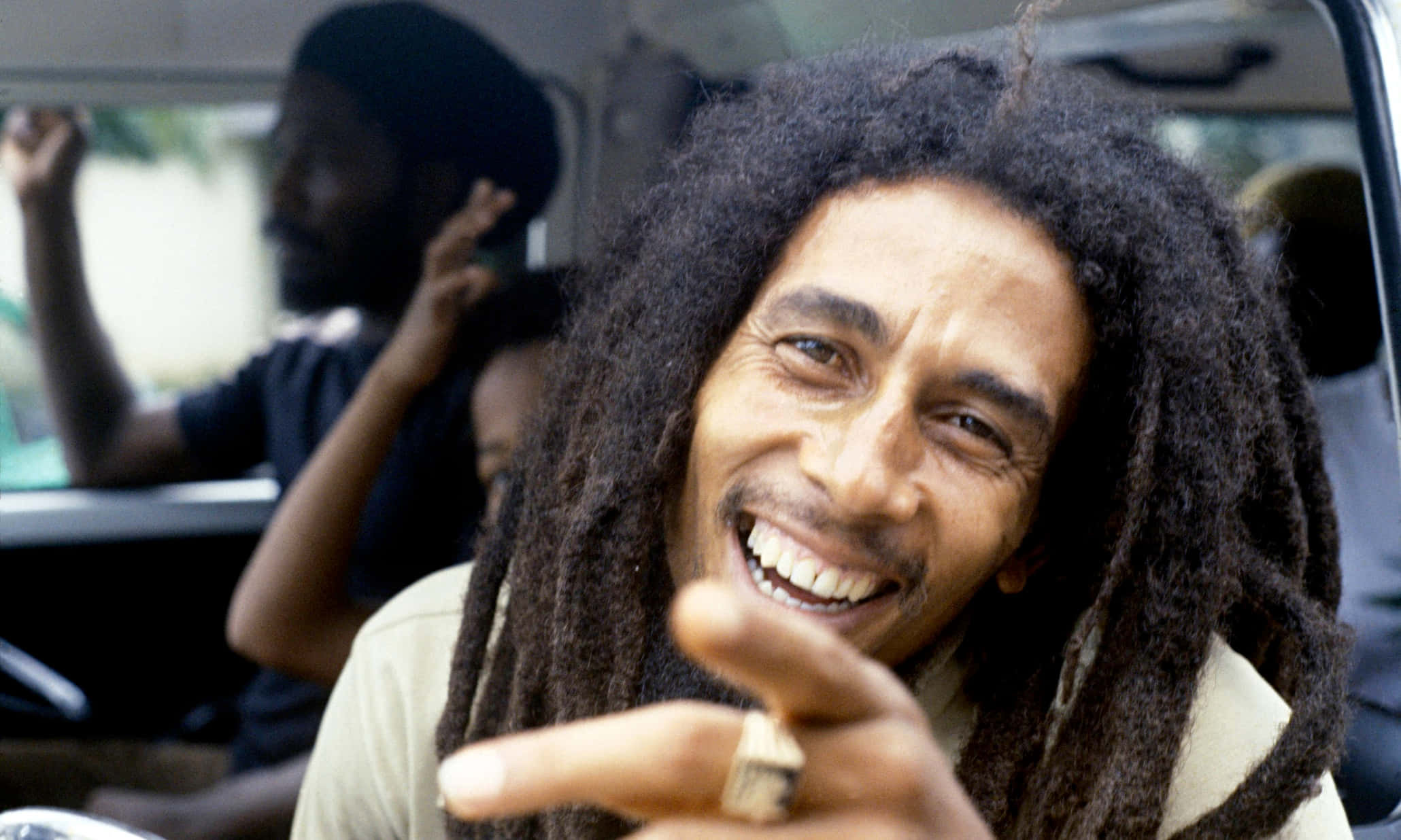 雷鬼之王——鮑勃·馬利 壁紙 — Bob Marley 喺車入面燦爛咁笑住指向鏡頭，表情充滿喜悅。
