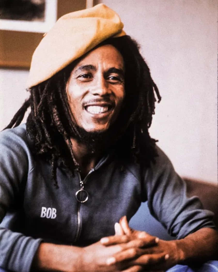 雷鬼之王鮑勃·馬利 壁紙 — Bob Marley 戴著米色貝雷帽和深色連帽衫，胸前繡有他的名字，溫暖地微笑。