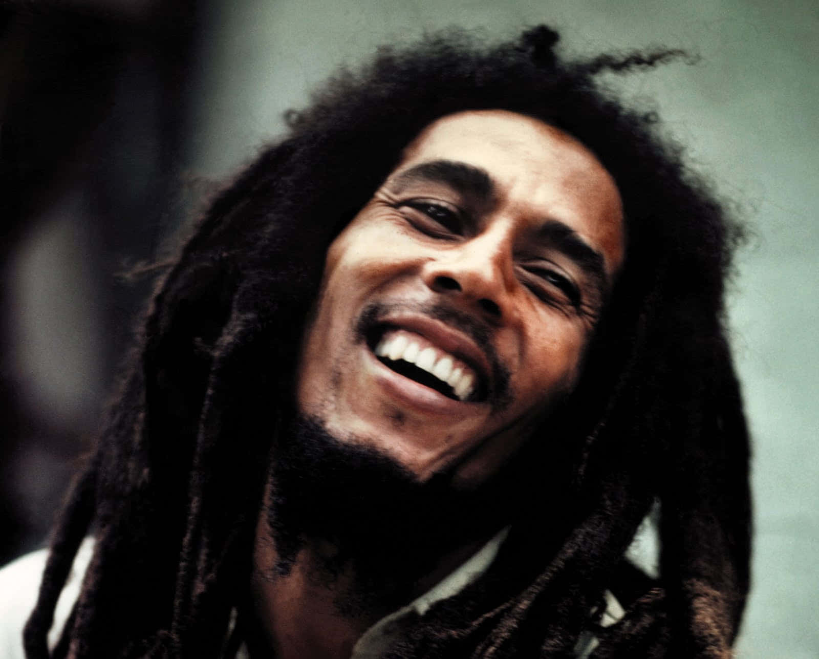 雷鬼傳奇人物——鮑勃·馬利 壁紙 — Bob Marley 愉快地大笑，他標誌性的辮子襯托出他燦爛的笑容。