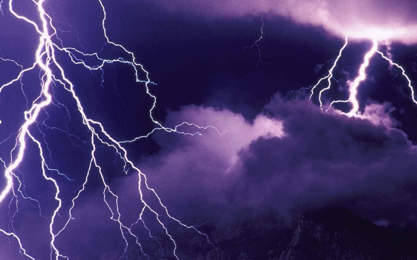 電光之 brilliance 壁紙 — 強烈的閃電在深紫色暴風雨天空中劈啪作響，掠過崎嶇的山峰。