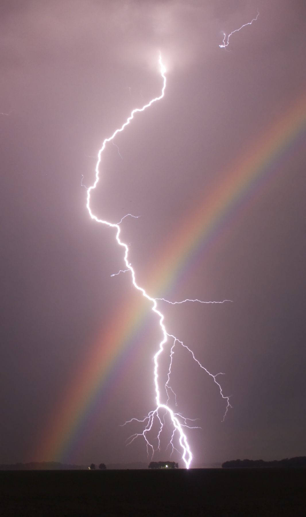 閃電在暴風雨的天空中擊中雙彩虹旁邊。