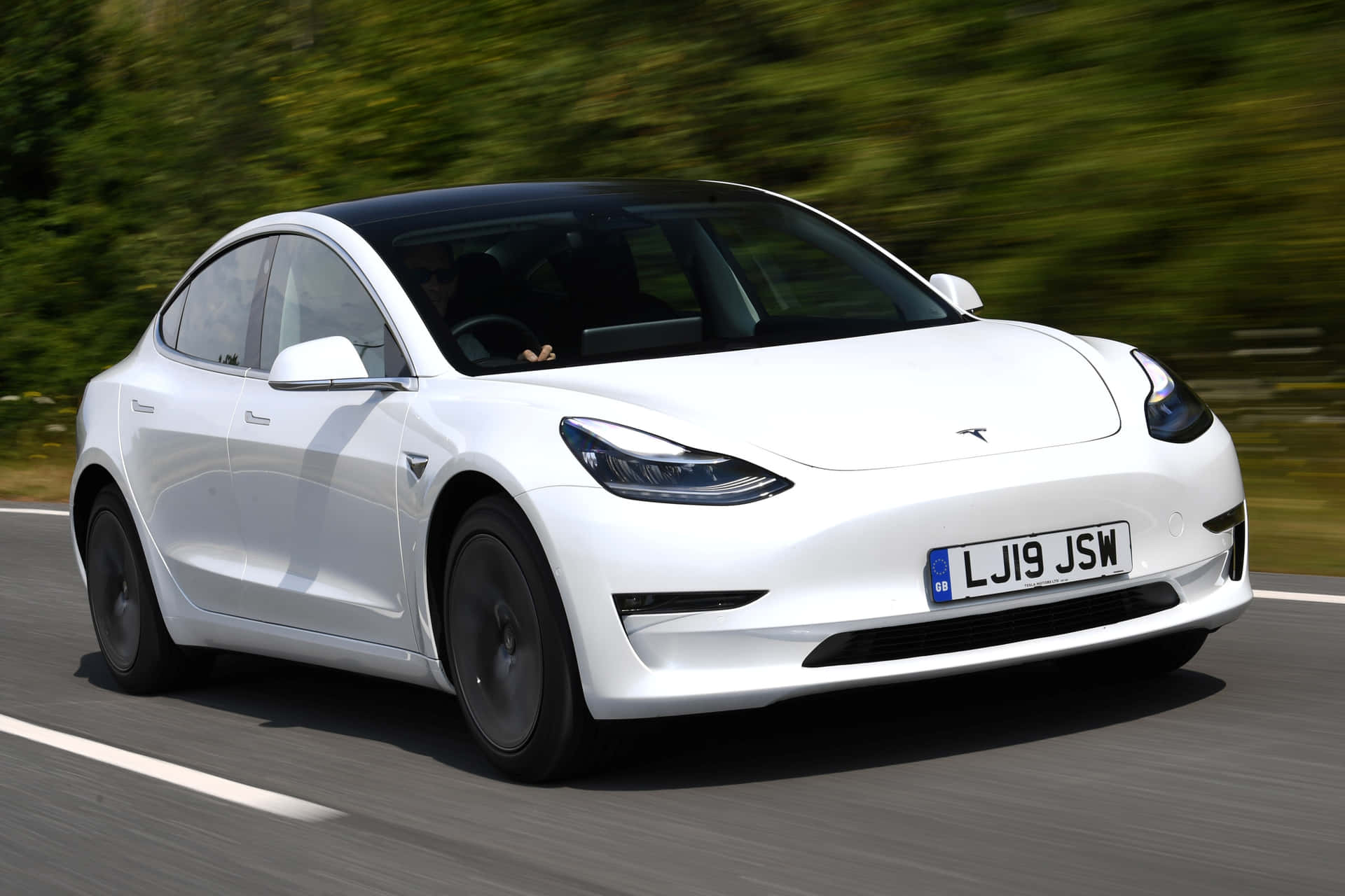 白色Tesla Model 3在道路上行駛，綠色樹木呈現動態模糊。