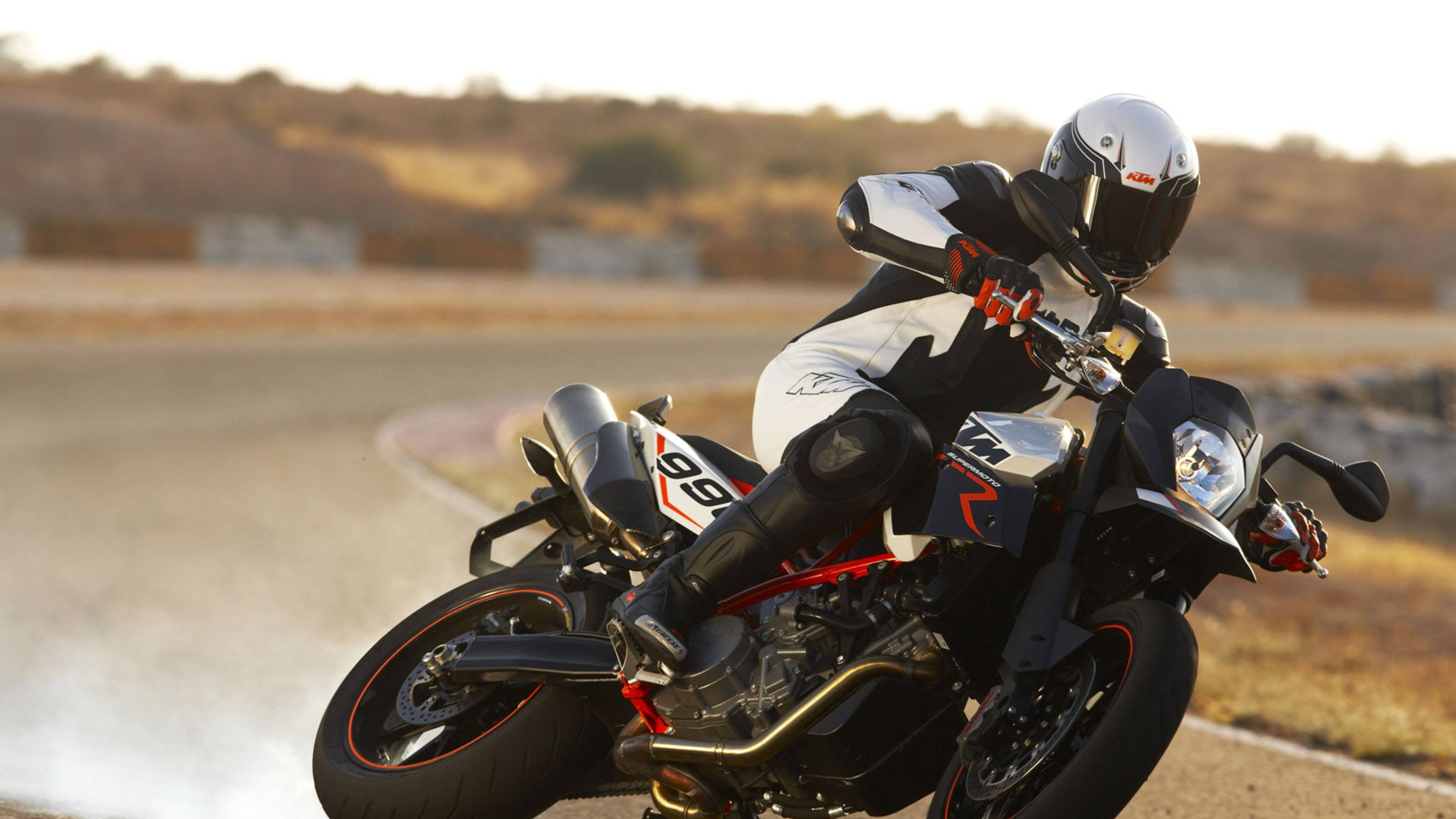 ktm rc 200 桌布 壁紙 — 電單車手在陽光普照的賽道上，騎著黑紅色跑車傾斜入一個急彎，揚起灰塵。