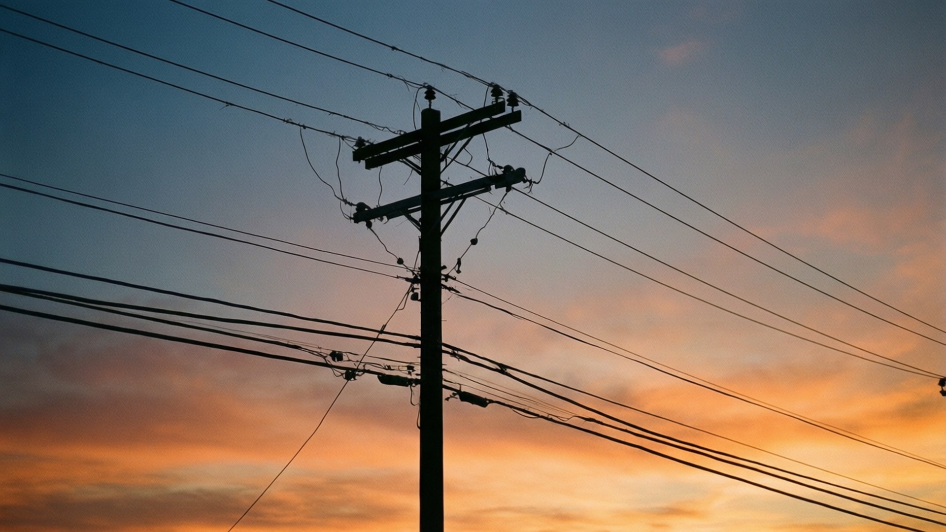 電報杆夕陽剪影 壁紙 — 木製電線桿的深色剪影，帶有縱橫交錯的電線，背景是充滿活力的日落天空，混合了橙色、粉紅色和藍色。