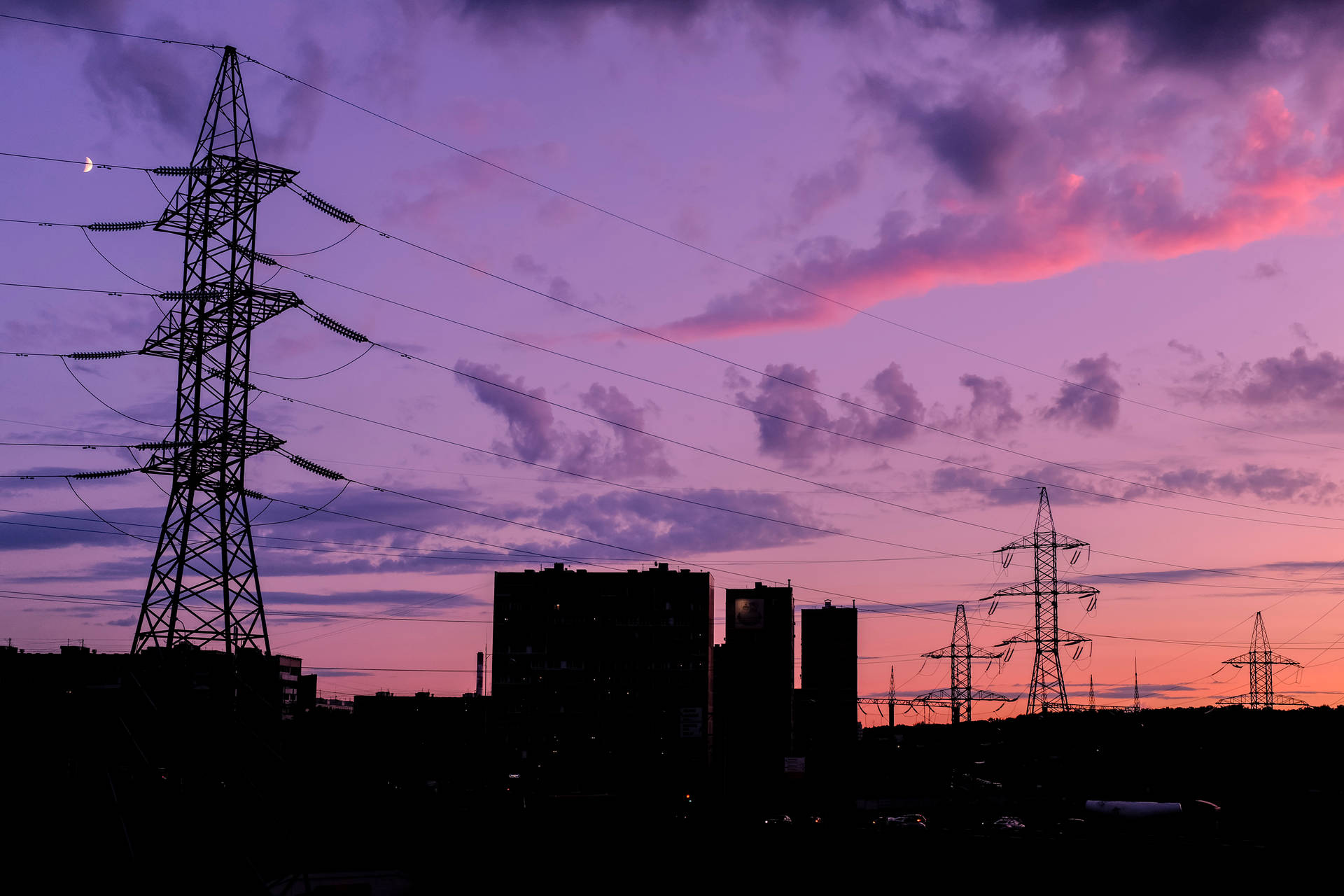 電線和建築物的剪影，襯托著色彩繽紛的暮色天空，伴隨著一彎新月。