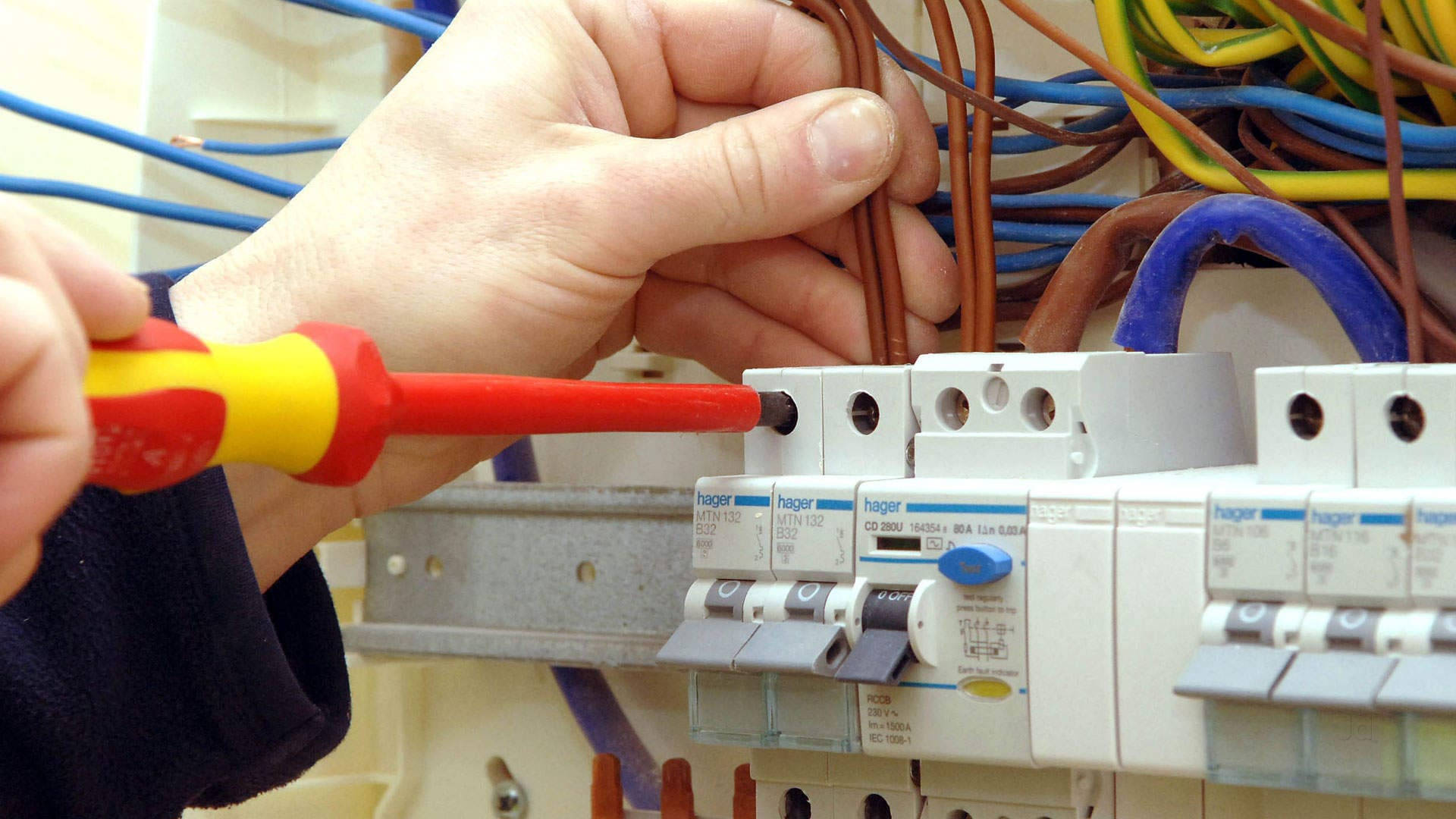 電工安裝開關 壁紙 — 雙手使用紅黃色螺絲批將電線連接到白色電路斷路器面板的特寫。