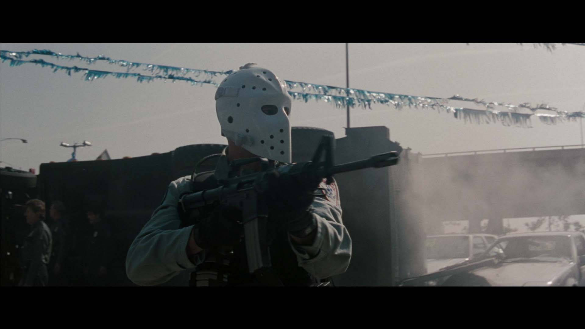 戴曲棍球面具的人手持步槍，在煙霧和閃粉的停車場中。