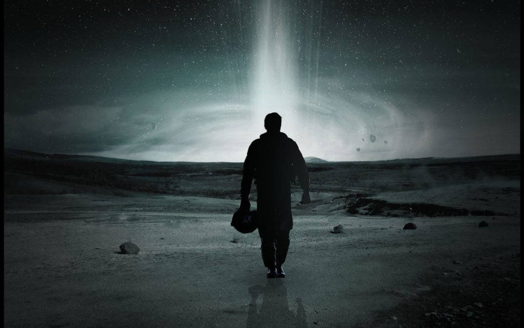 電影《星际穿越》中的宇航員 壁紙 — 一個孤獨的身影在黑暗的天空下，走向星際外星景觀中一個發光的宇宙傳送門。