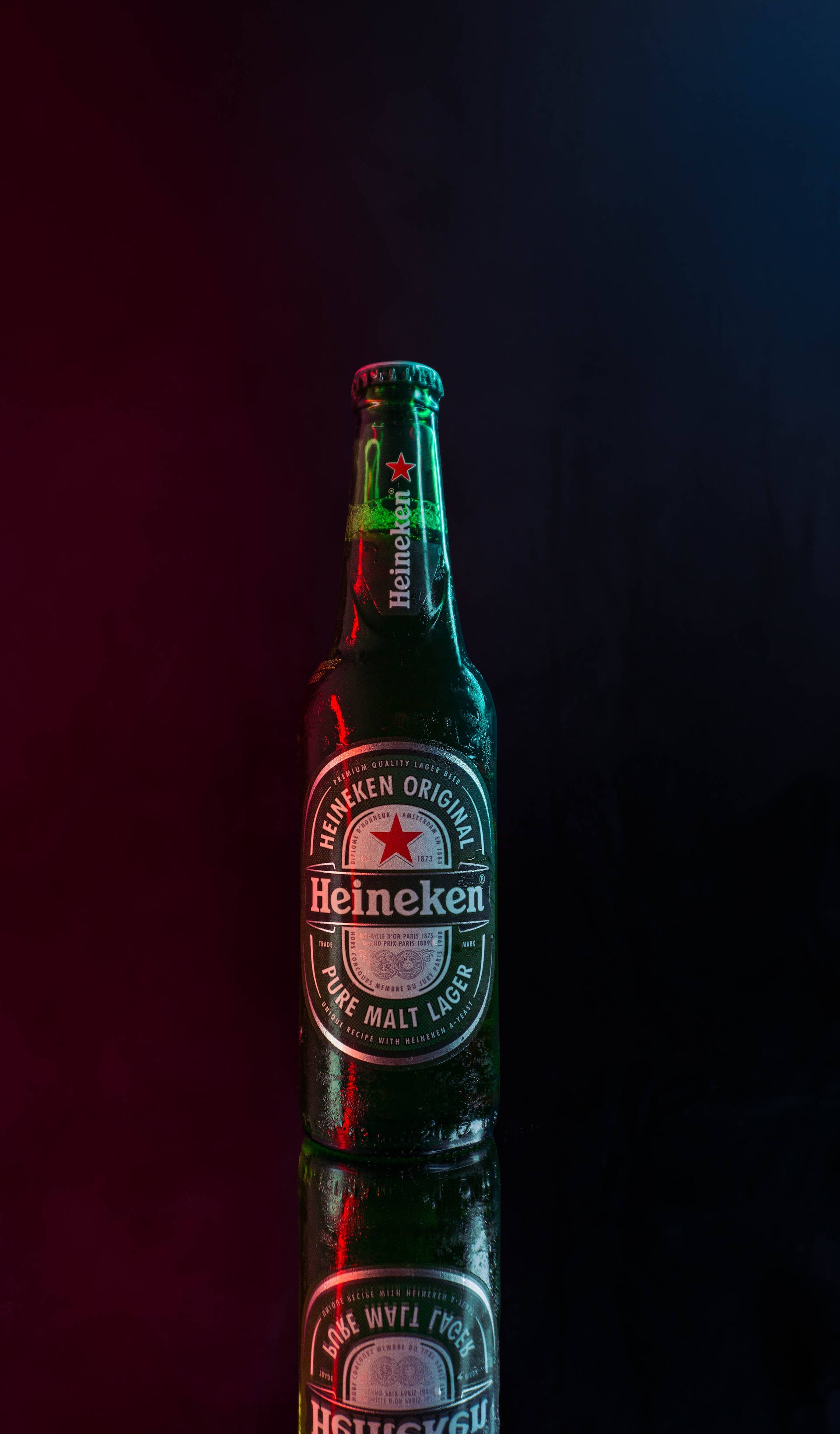 電影感背景下的喜力啤酒瓶 壁紙 — 一支冰凍的喜力啤酒瓶在深色背景下，於戲劇性的紅藍燈光照射下豎立在反光表面上。