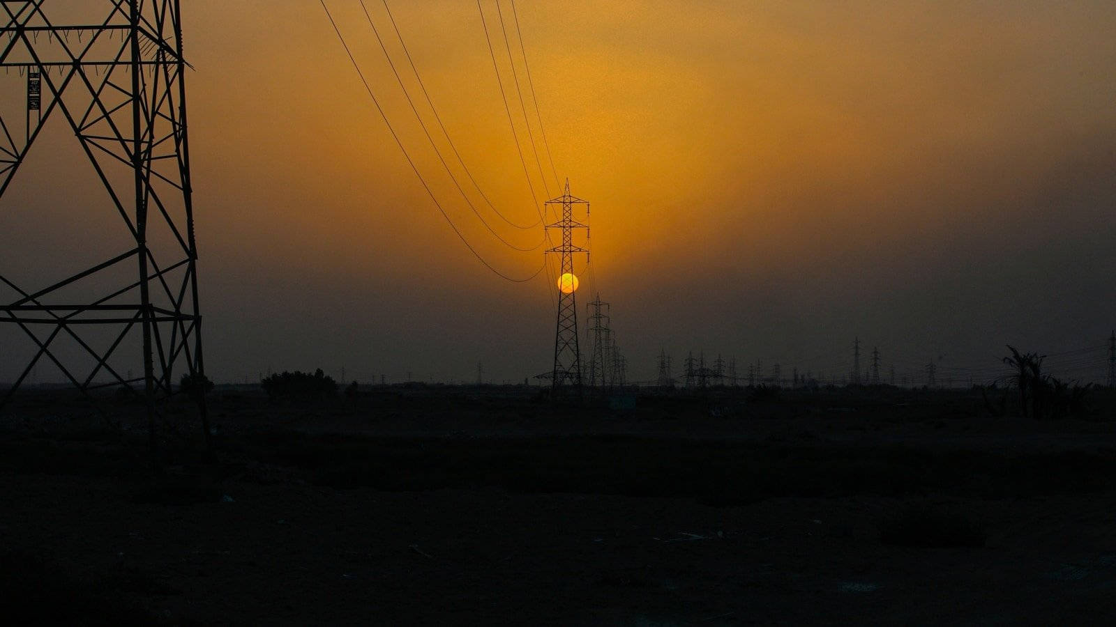 輸電塔在發光的橙色夕陽天空下呈現剪影。