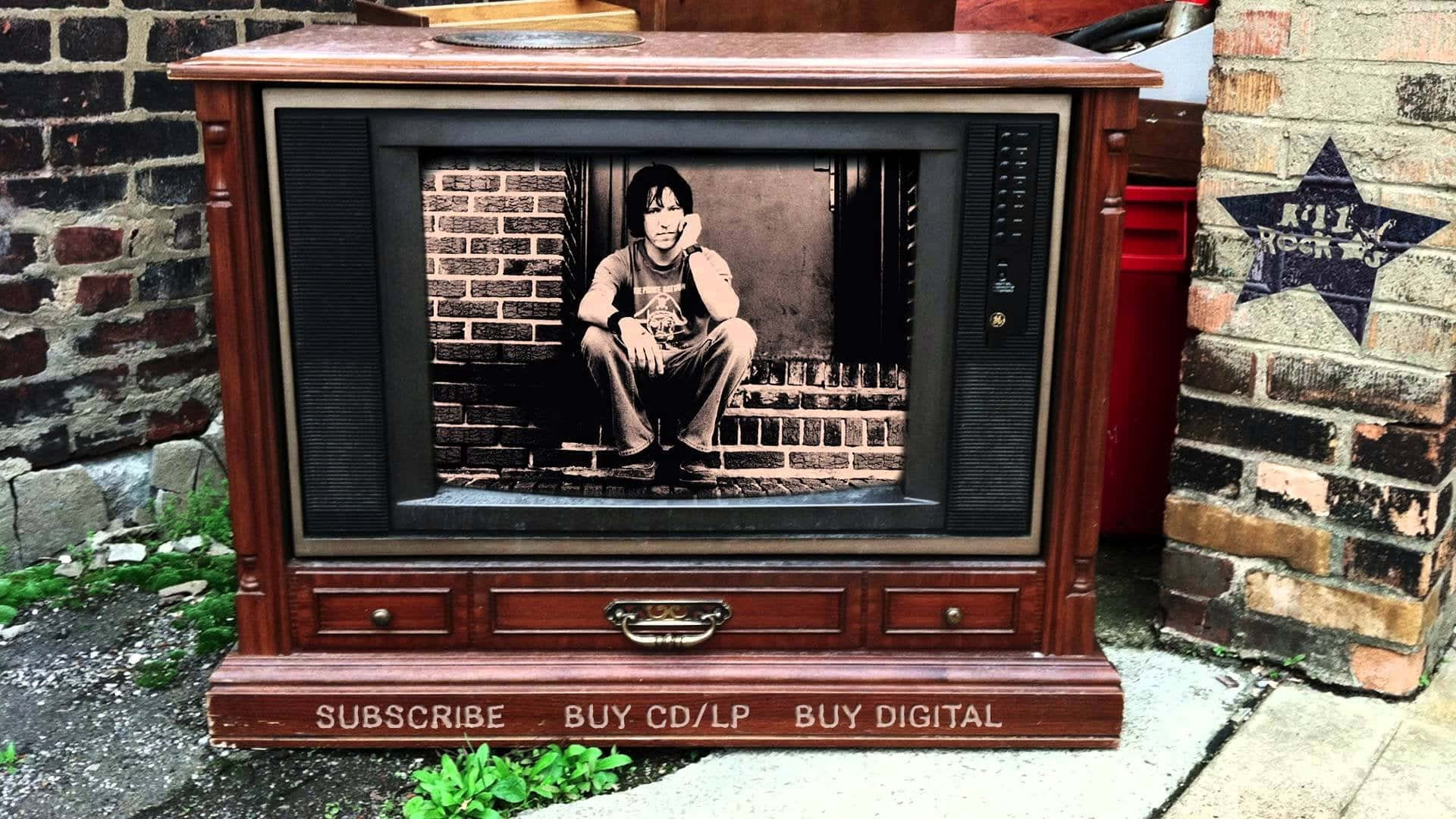 復古木製電視櫃，附有磚階上人物的照片和「subscribe buy cd lp buy digital」文字。