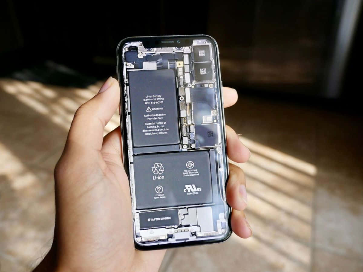 手拿著一部在陽光下內部電池和電路外露的電話。