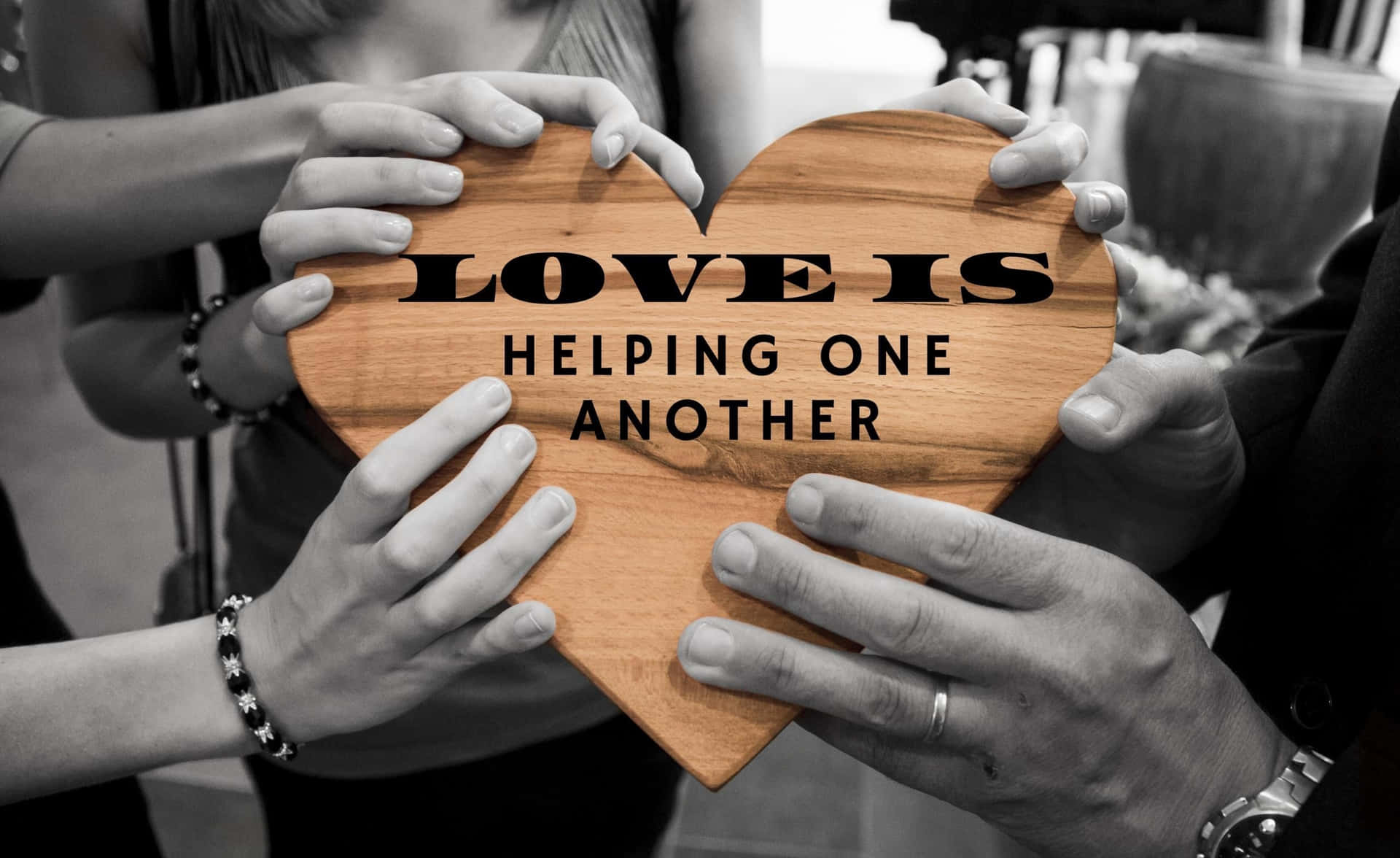 多隻手托住一個木製心形，上面有「Love is helping one another」的訊息。