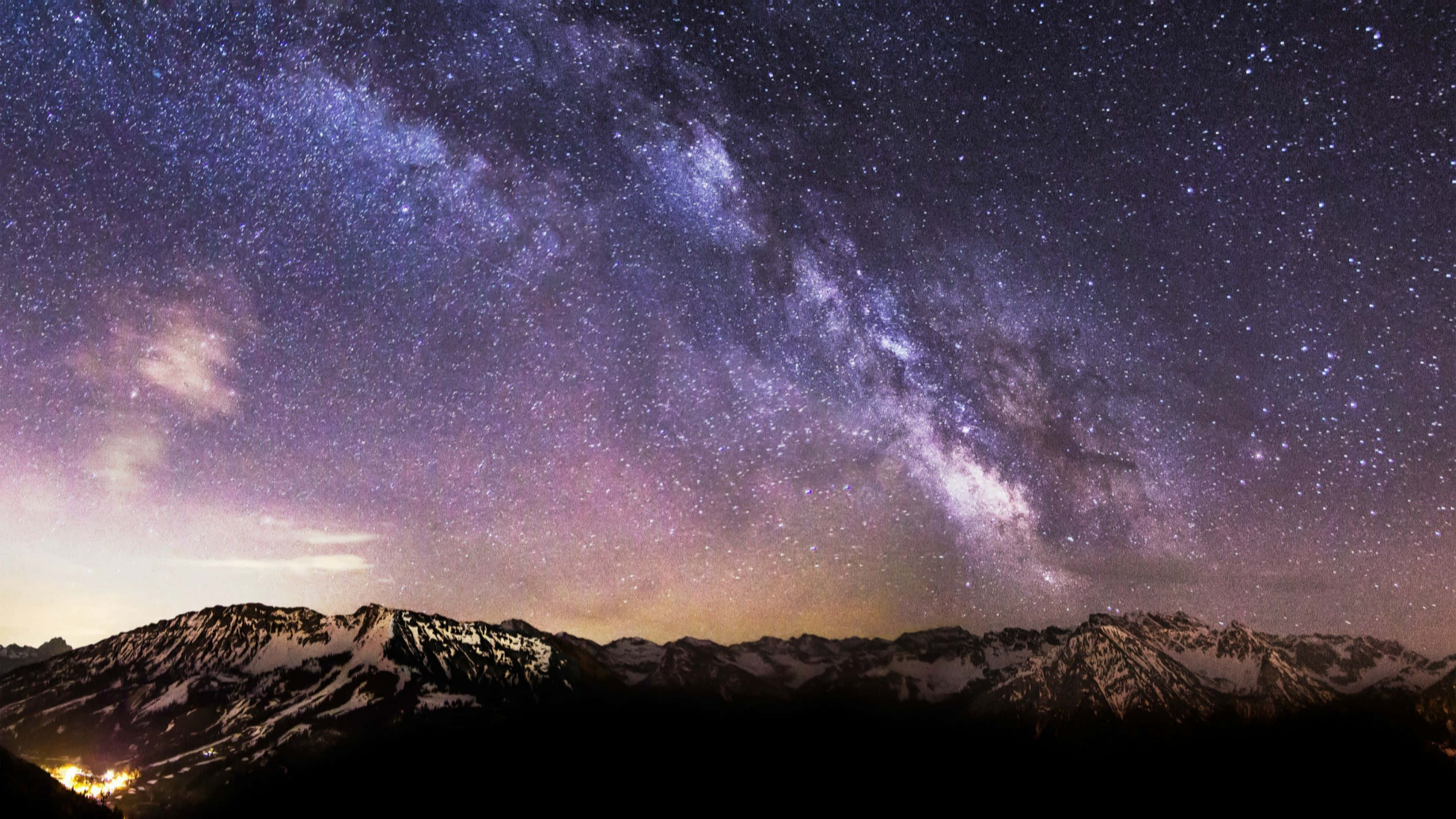 震撼的 UHD 風景攝影 壁紙 — 銀河系在紫色和藍色色調的星空下，拱形跨越積雪的山峰。