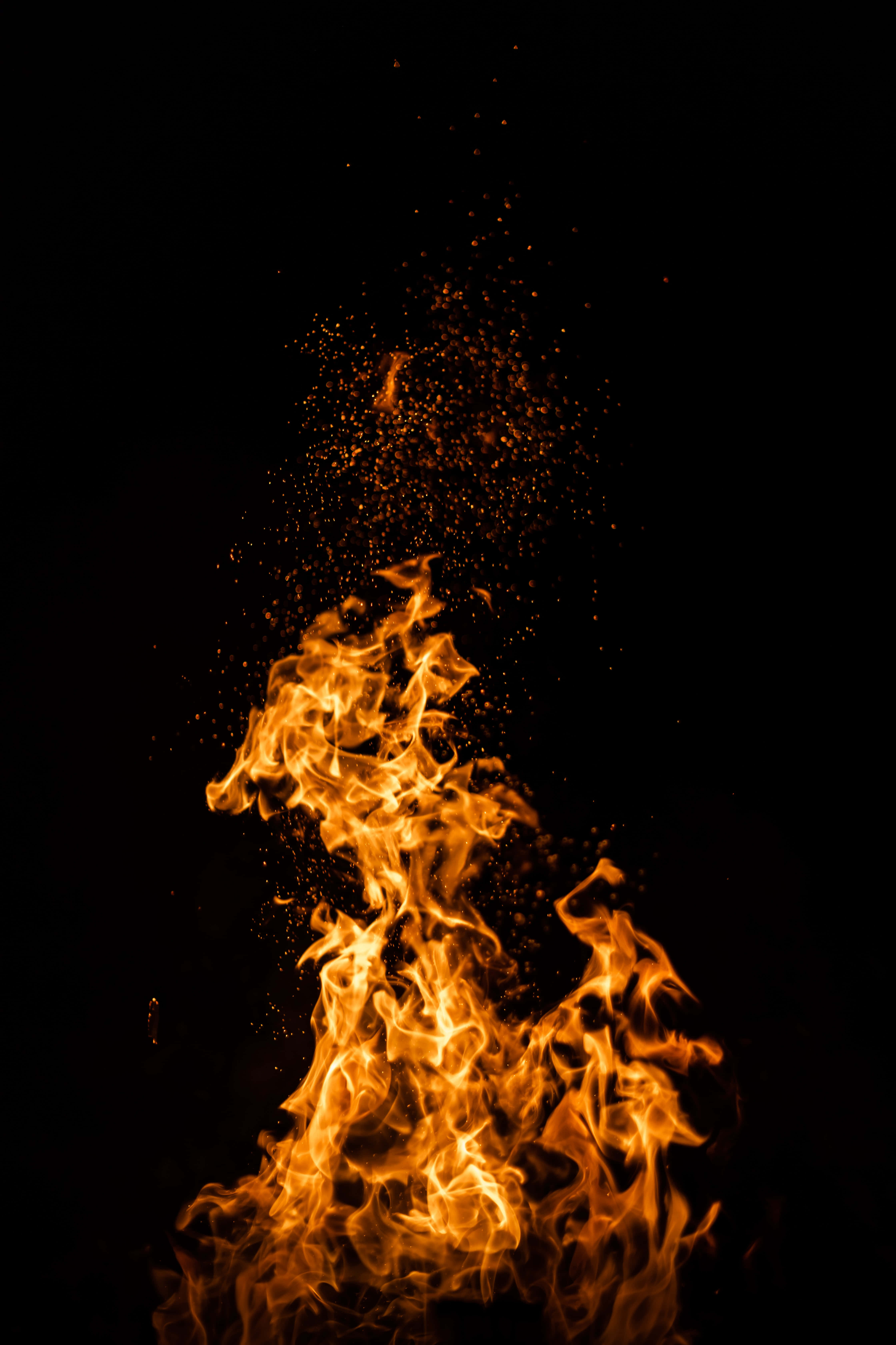 震撼真實火焰 iPhone 背景 壁紙 — 鮮豔的橙色火焰在純黑色背景上向上爆發，發光的餘燼向上飄散。