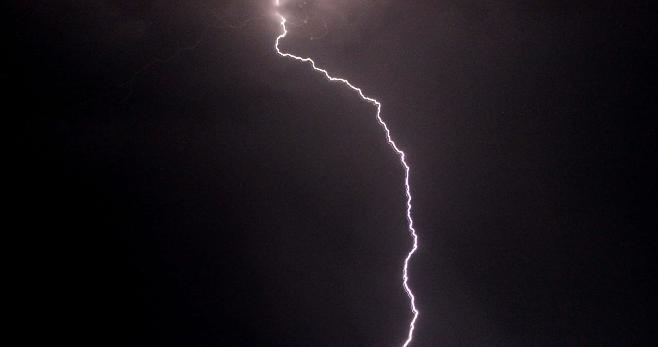 震撼雷暴秀 壁紙 — 一道鋸齒狀的閃電在漆黑的暴風雨天空中叉開，帶有強烈的白色和紫色色調。