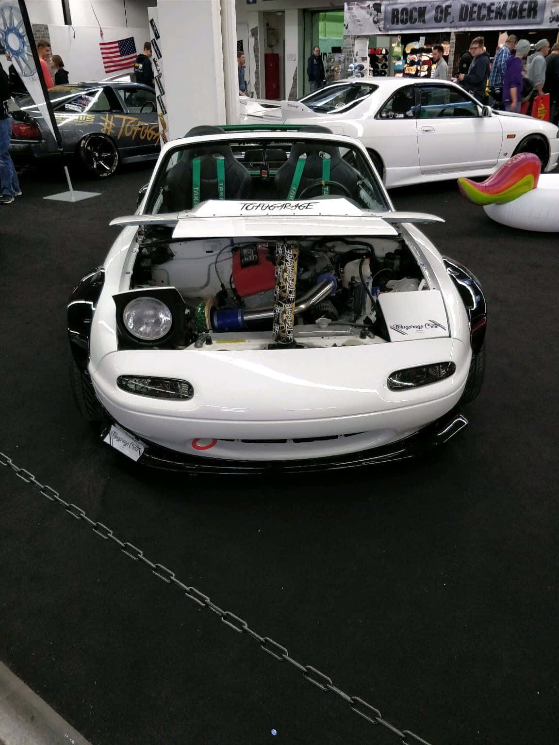震撼馬自達MX-5 Miata — 開放力量與優雅 壁紙 — 一輛白色改裝的萬事得MX-5，引擎蓋打開展示定制引擎，在室內車展中展出，背景有人群和其他車輛。