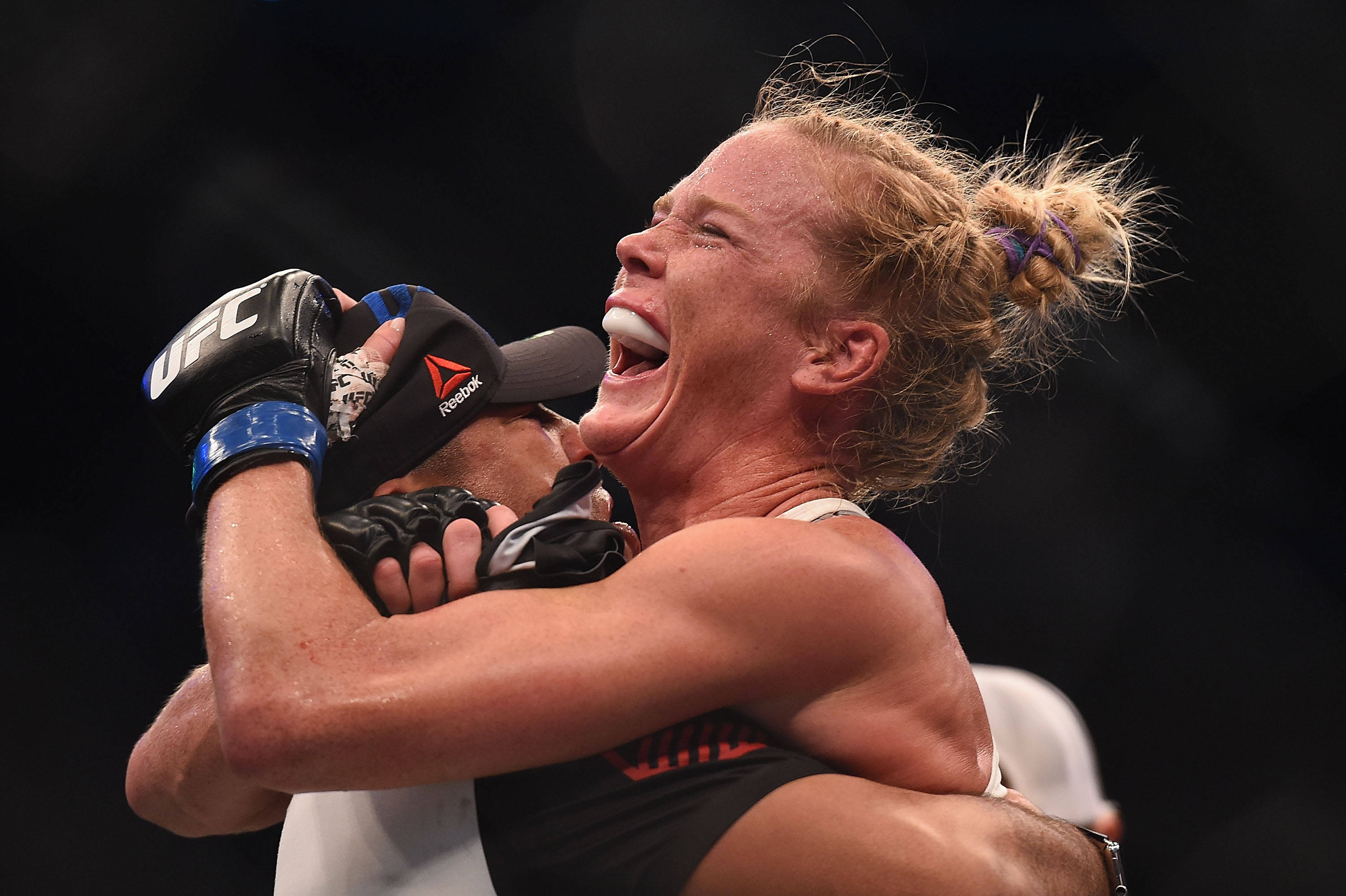 霍莉·霍姆贏得UFC 193 壁紙 — 一位戴著黑色UFC手套的女拳手在比賽後以勝利的、充滿情感的擁抱擁抱對手。