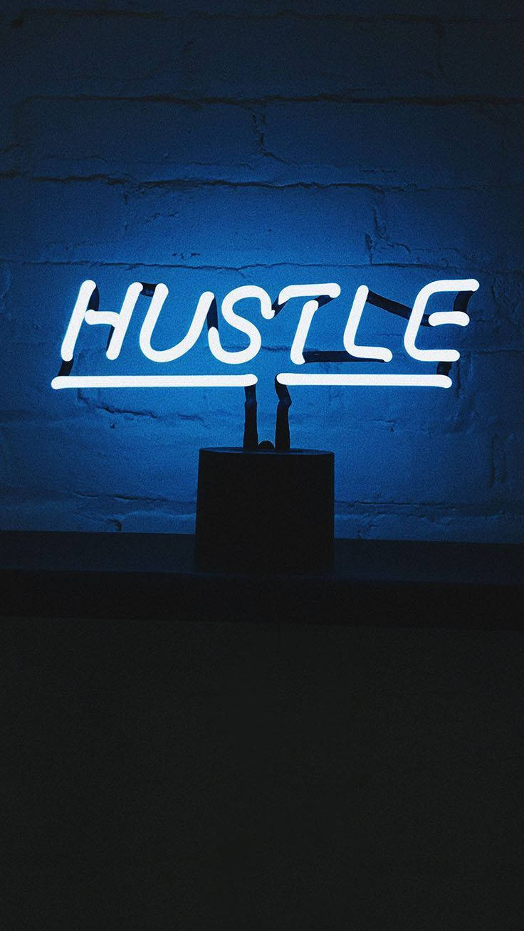 霓虹奮鬥風 iPhone 壁紙 — 一個發光的白色霓虹燈牌，拼寫著 HUSTLE，在昏暗的空間中對著紋理磚牆投射出冷藍色的光芒。