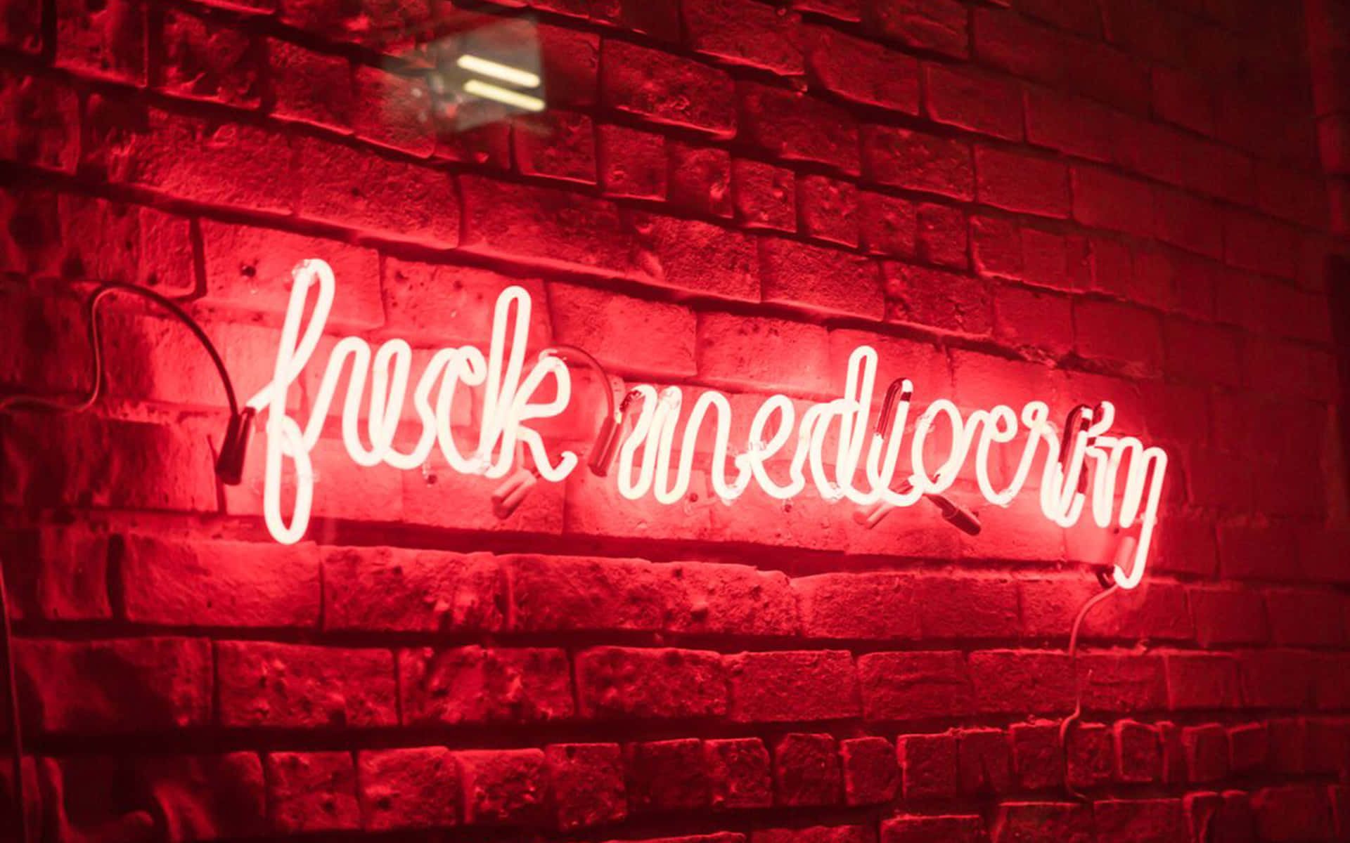 夜間磚牆上寫著「fuck mediocrity」的紅色霓虹燈牌。