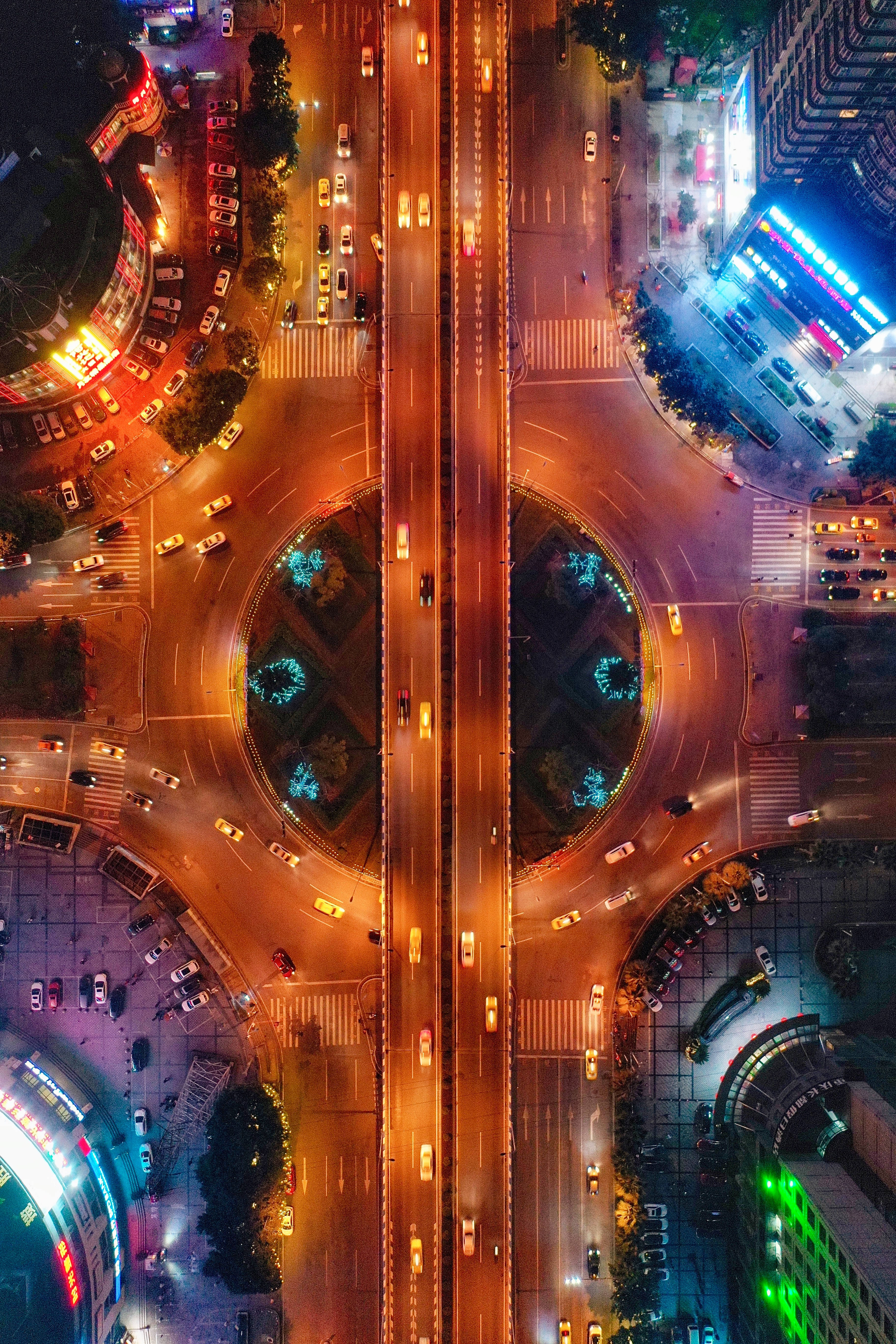霓虹汽車鳥瞰圖 壁紙 — 繁忙城市交叉口的夜間空中景觀，帶有發光路燈和行駛中的汽車。