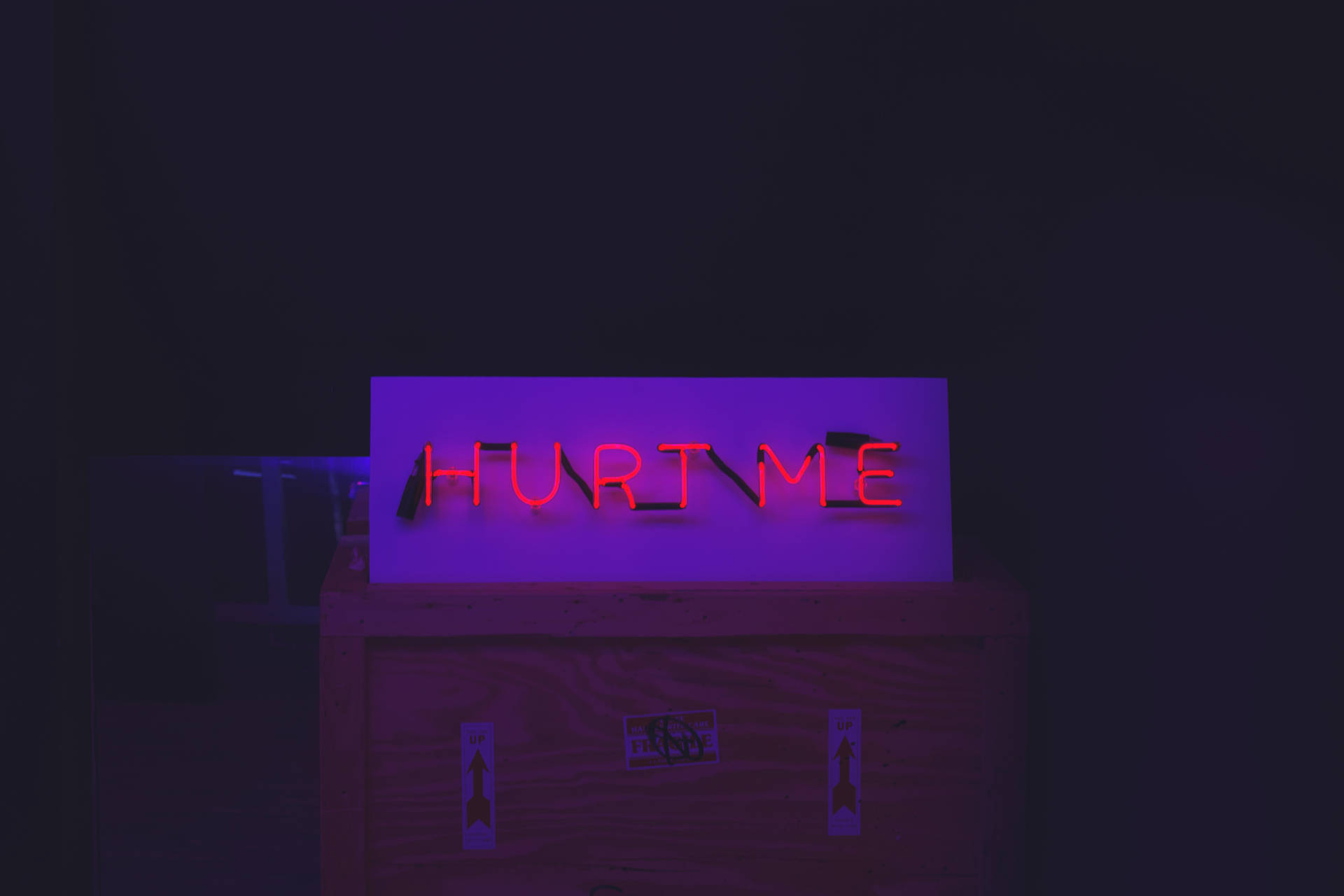 黑暗房間中木箱上寫著 hurt me 的紅色霓虹燈牌。