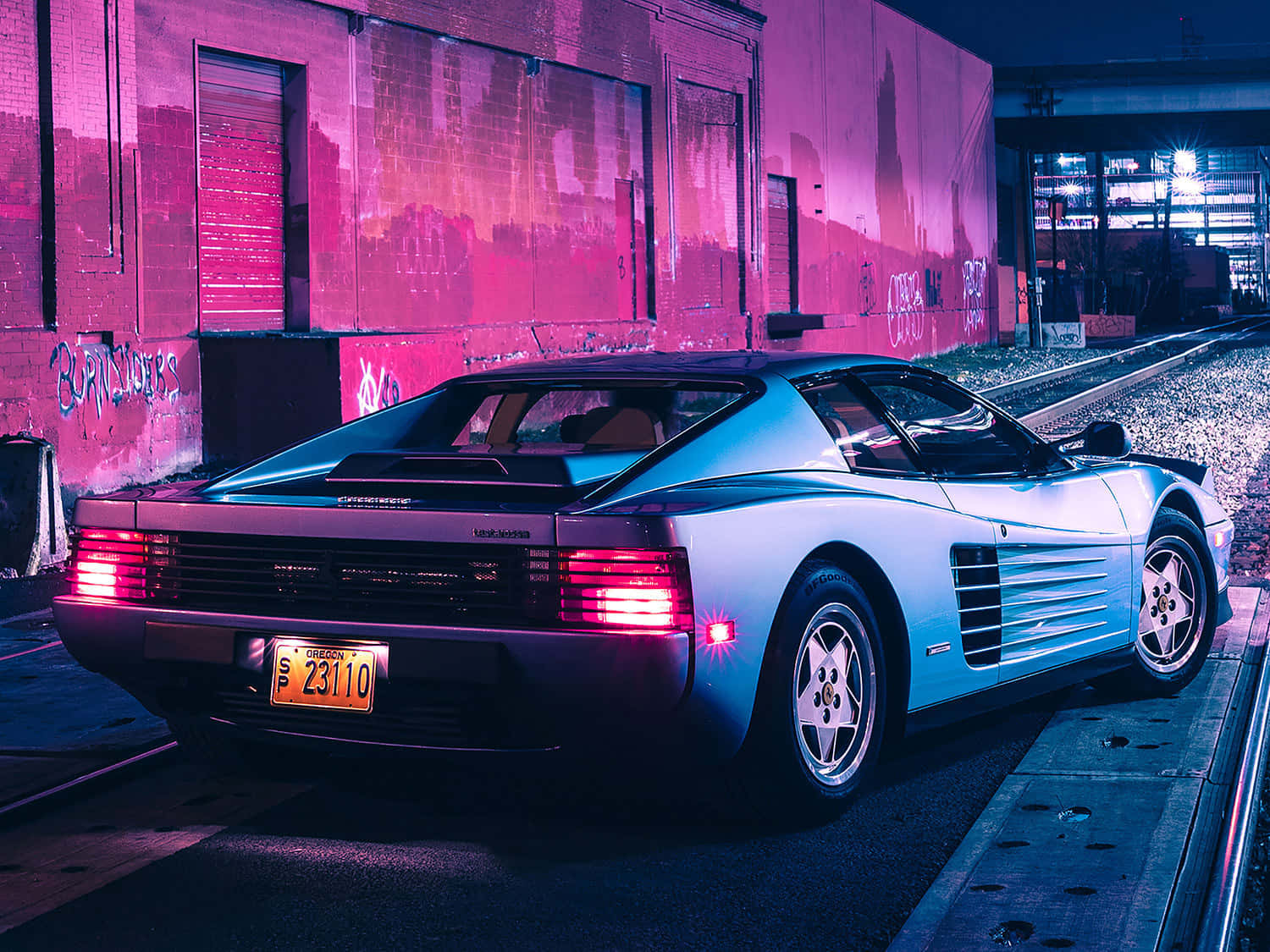 銀色法拉利 Testarossa 夜間停泊在火車軌道旁，在霓虹燈下。