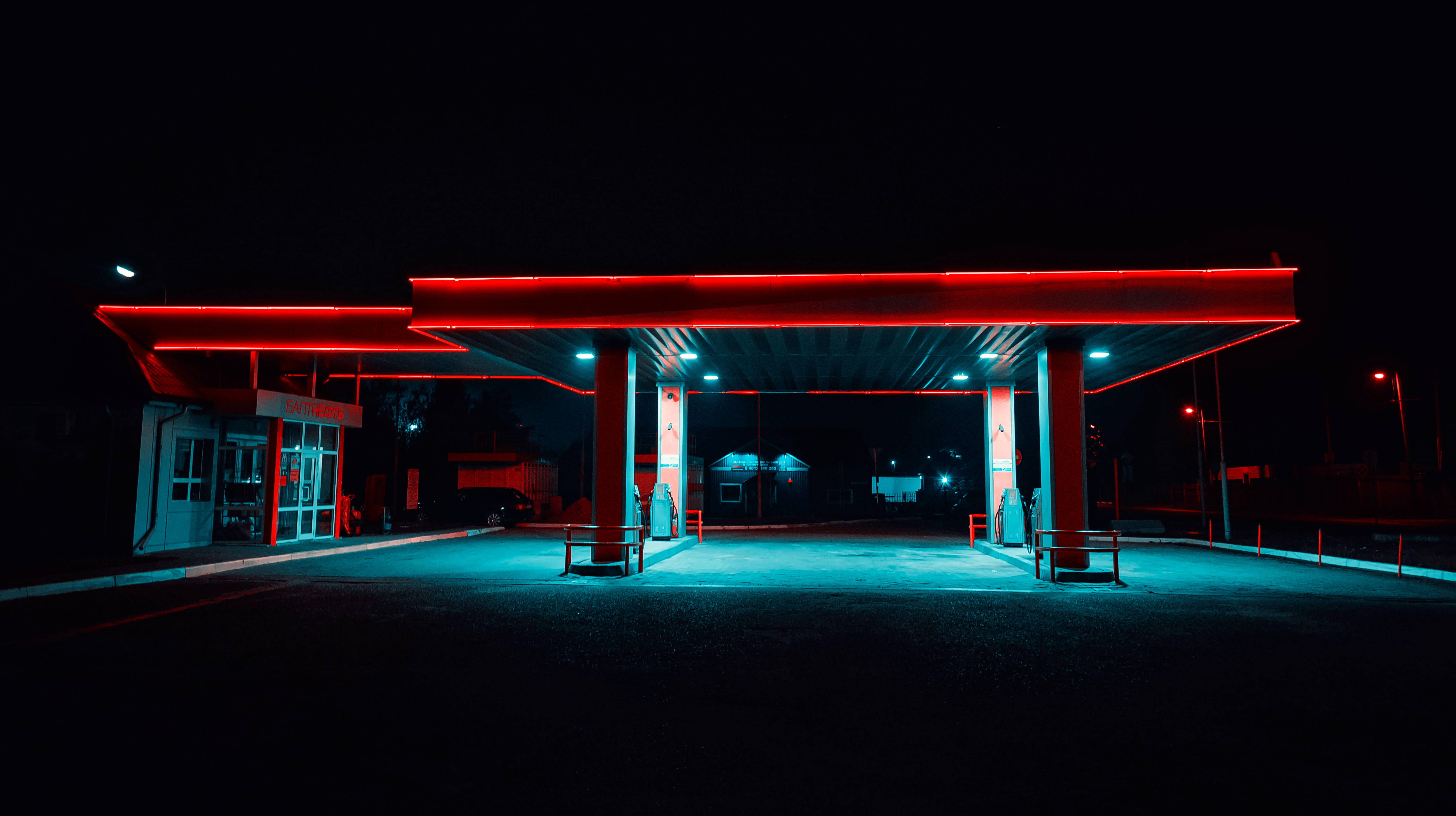 霓虹燈加油站 壁紙 — 夜晚被霓虹燈照亮的加油站，紅色和藍色的燈光在空油泵和黑暗的路面上投射出戲劇性的光芒。
