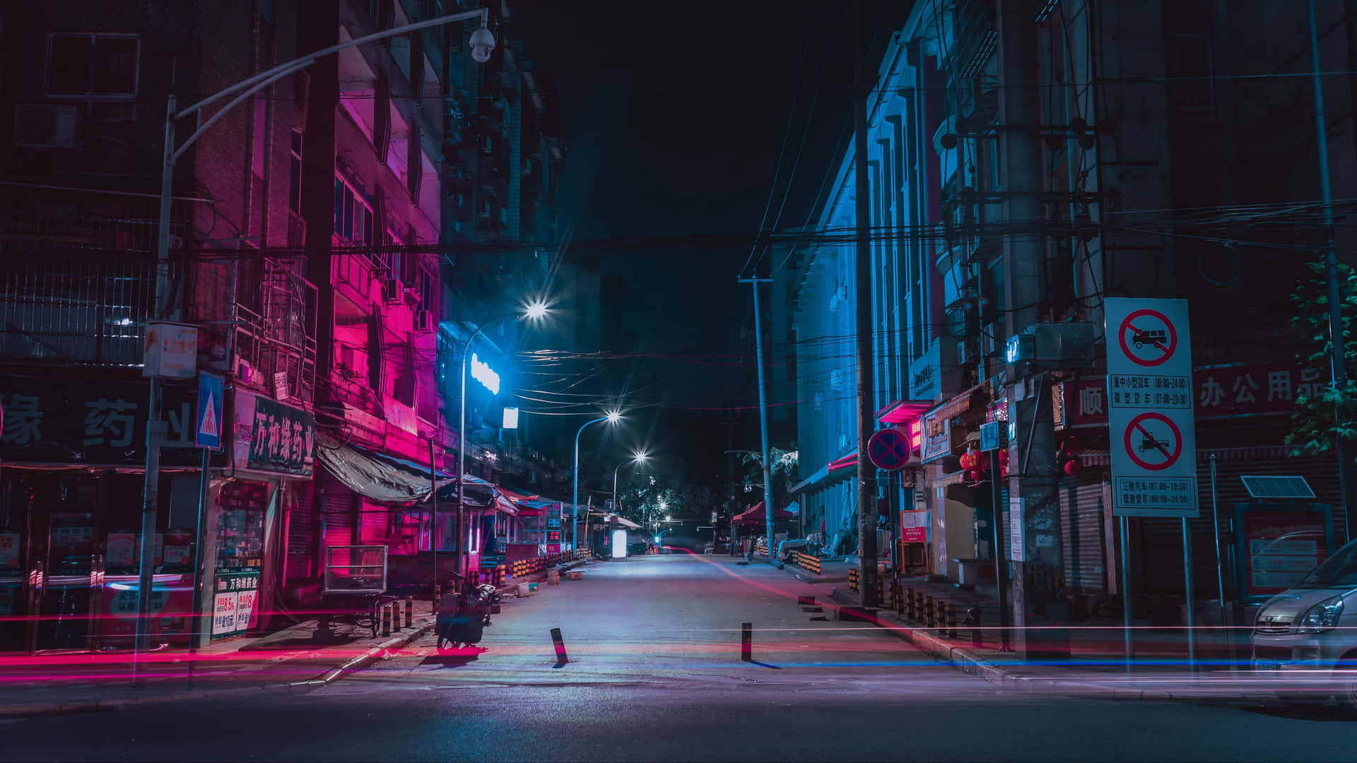 夜晚霓虹燈照亮的空蕩街道，濕漉漉路面上有粉紅色和藍色的反射。