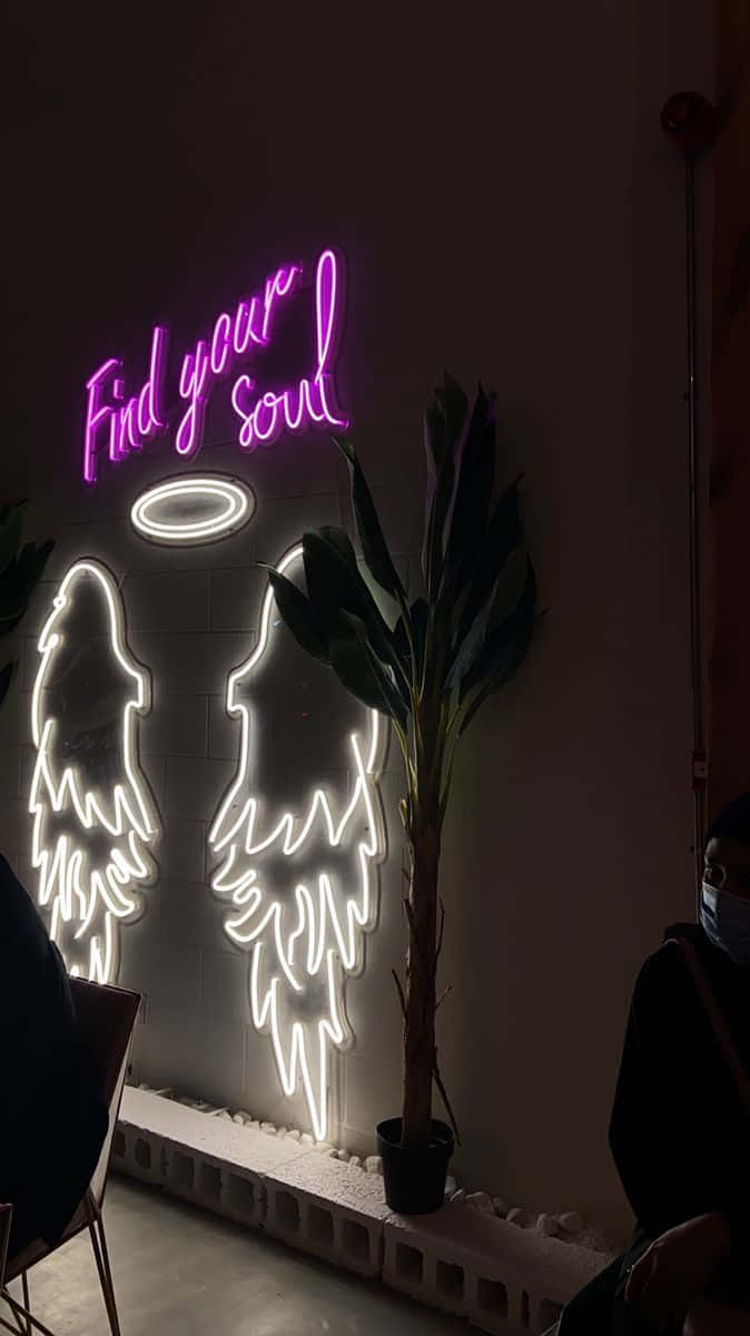 霓虹燈牌寫著「Find your soul」，帶有天使剪影和光環，在一個黑暗的房間裡，旁邊有一棵植物。