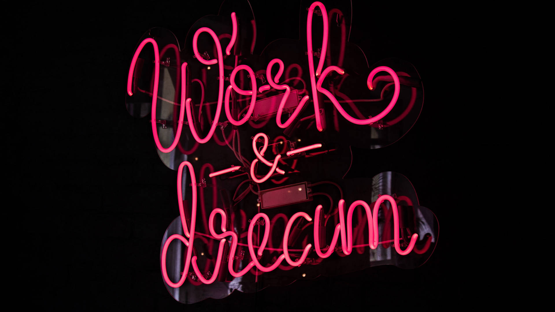 黑暗反光表面上的粉紅色霓虹燈牌，寫著 Work & Dream