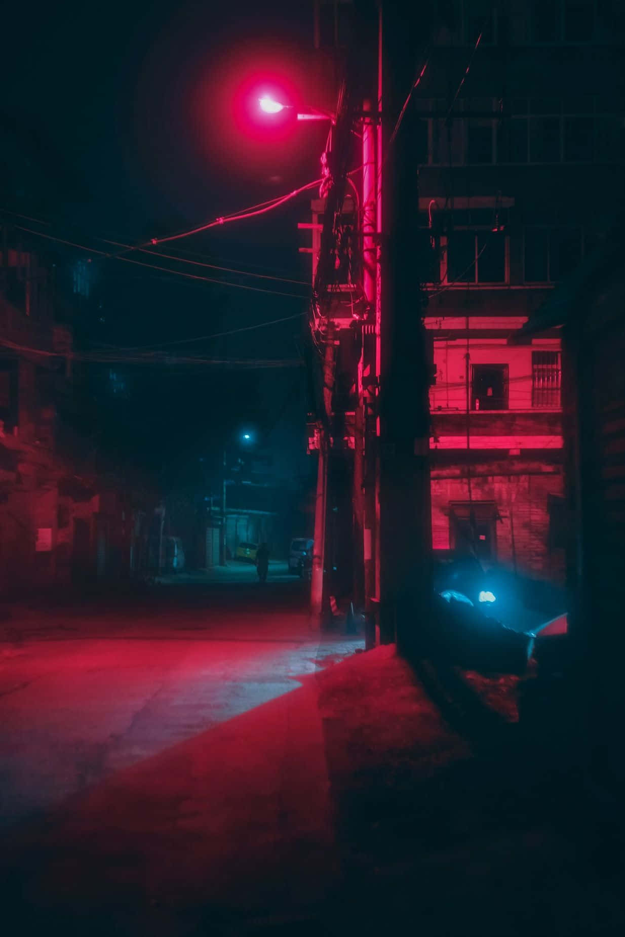 夜晚紅光照亮的小巷，有建築物和架空電線。