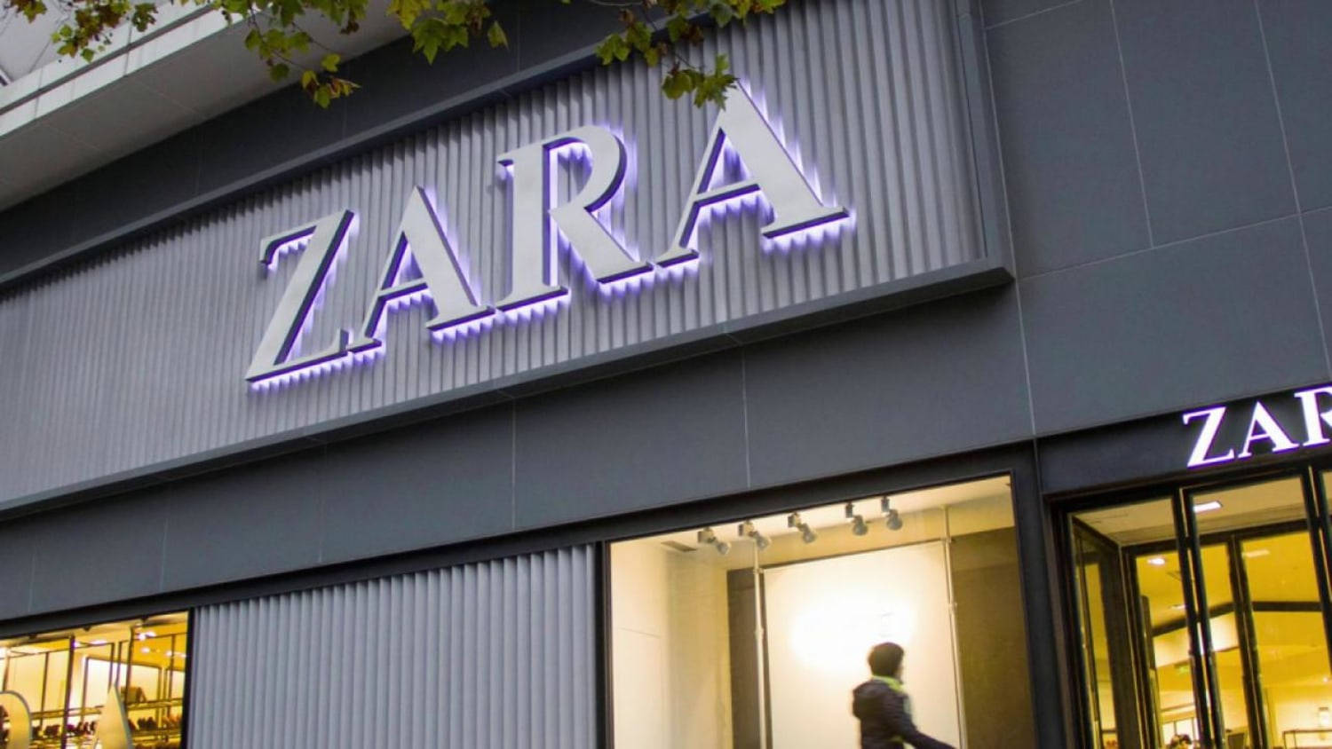 霓虹紫光Zara招牌 壁紙 — 現代Zara商店外牆，灰色波紋板及玻璃窗上帶有發光的紫色霓虹燈標誌。