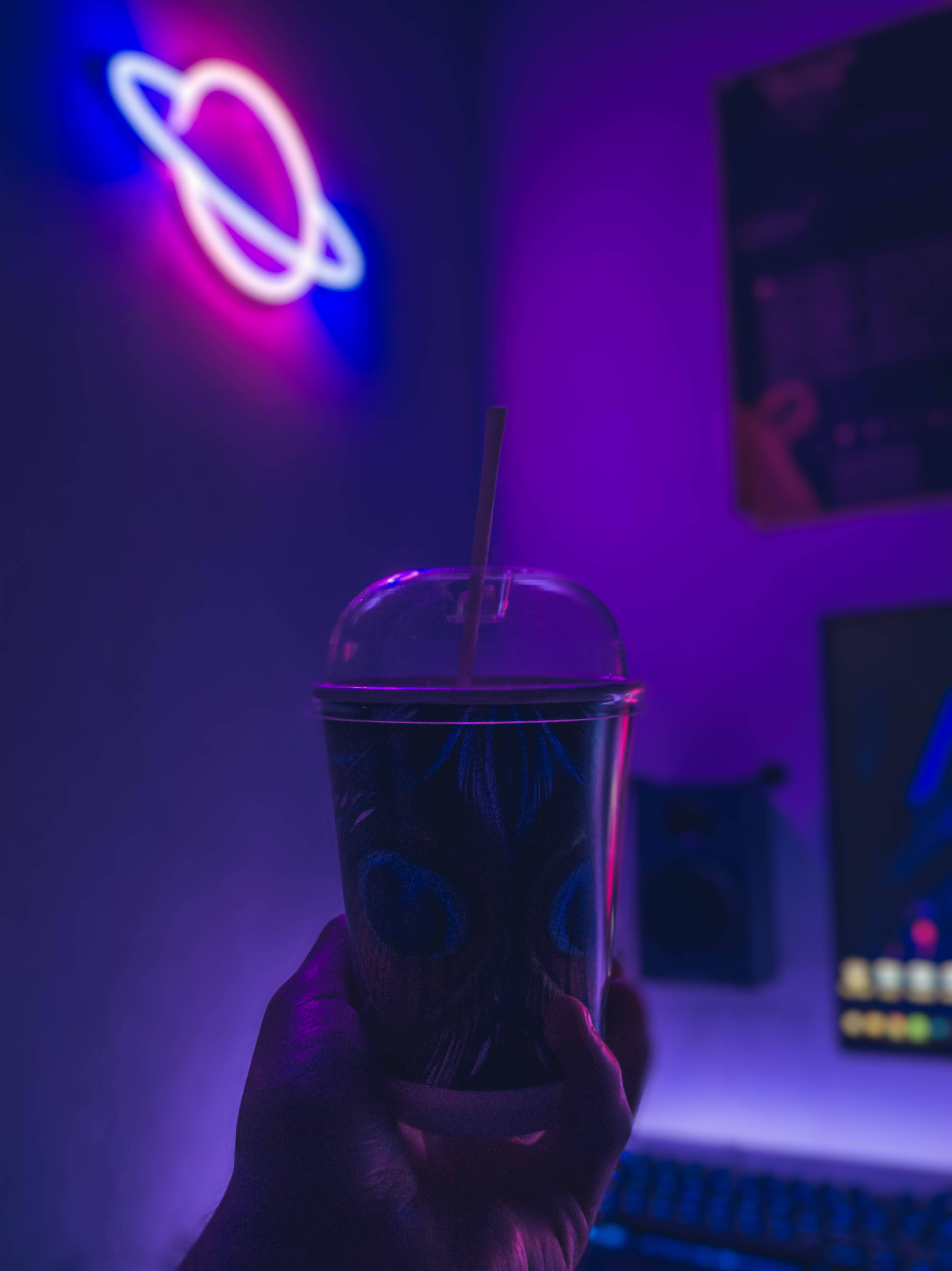 霓虹紫調LED燈牌 壁紙 — 一隻手在充滿未來感的遊戲室中，在鮮豔的紫色和粉紅色霓虹燈光下拿著發光的飲料。